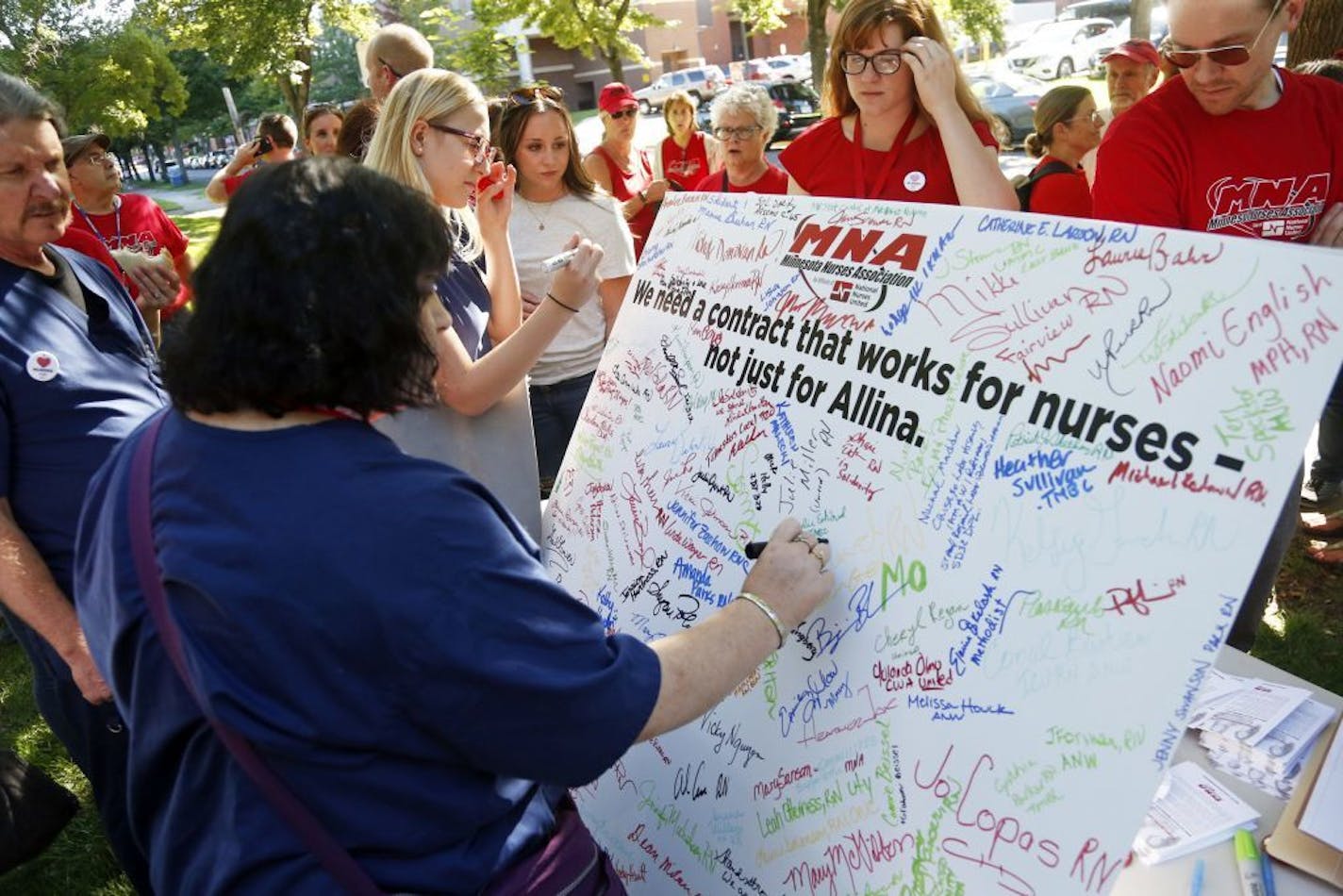 A nurse adds her signature to scores of signatures that fill a large poster of the Minnesota Nurses Associations as community, labor leaders and faith-based groups gather at Stewart Park Wednesday, Aug. 31, 2016 in Minneapolis for a rally to show support for Allina Health nurses who are scheduled to go on strike Monday, Sept. 5, unless a settlement is reached.