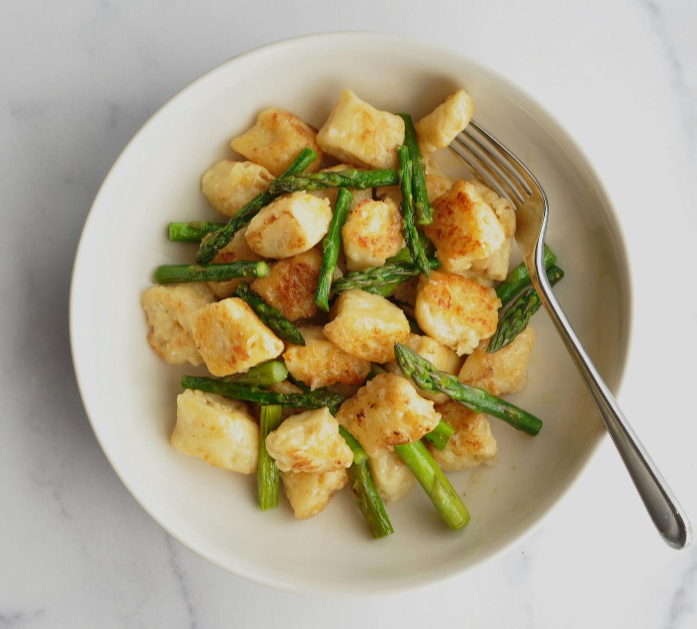 A bowl of cheesy dumplings with asparagus in a lemon-brown butter sauce.