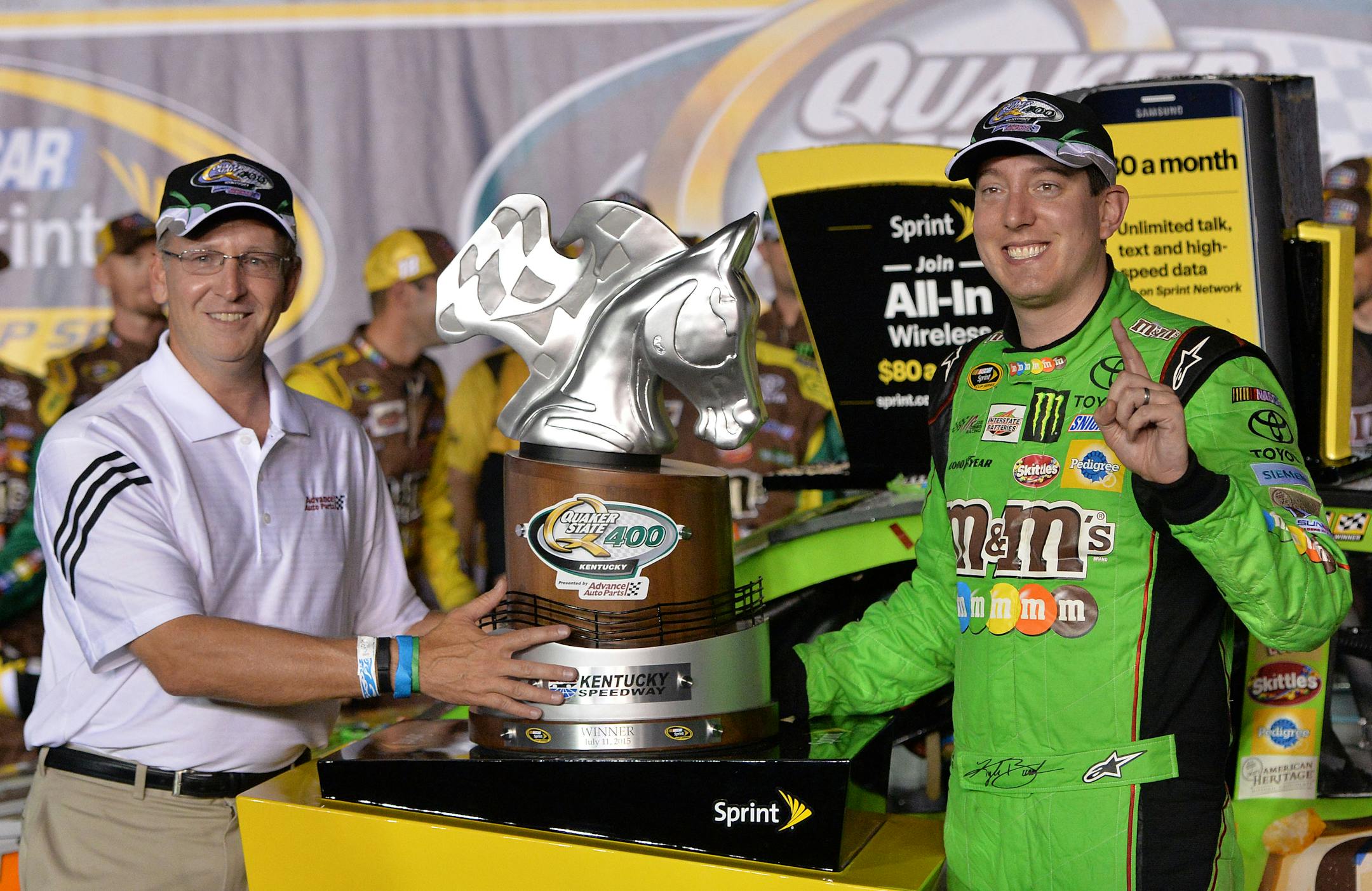 Kyle Busch, right, accepts the trophy from Advanced Auto Parts President Joe Sherman following his victory in the NASCAR Sprint Cup series auto race at Kentucky Speedway in Sparta, Ky., Saturday, July 11, 2015. (AP Photo/Timothy D. Easley)