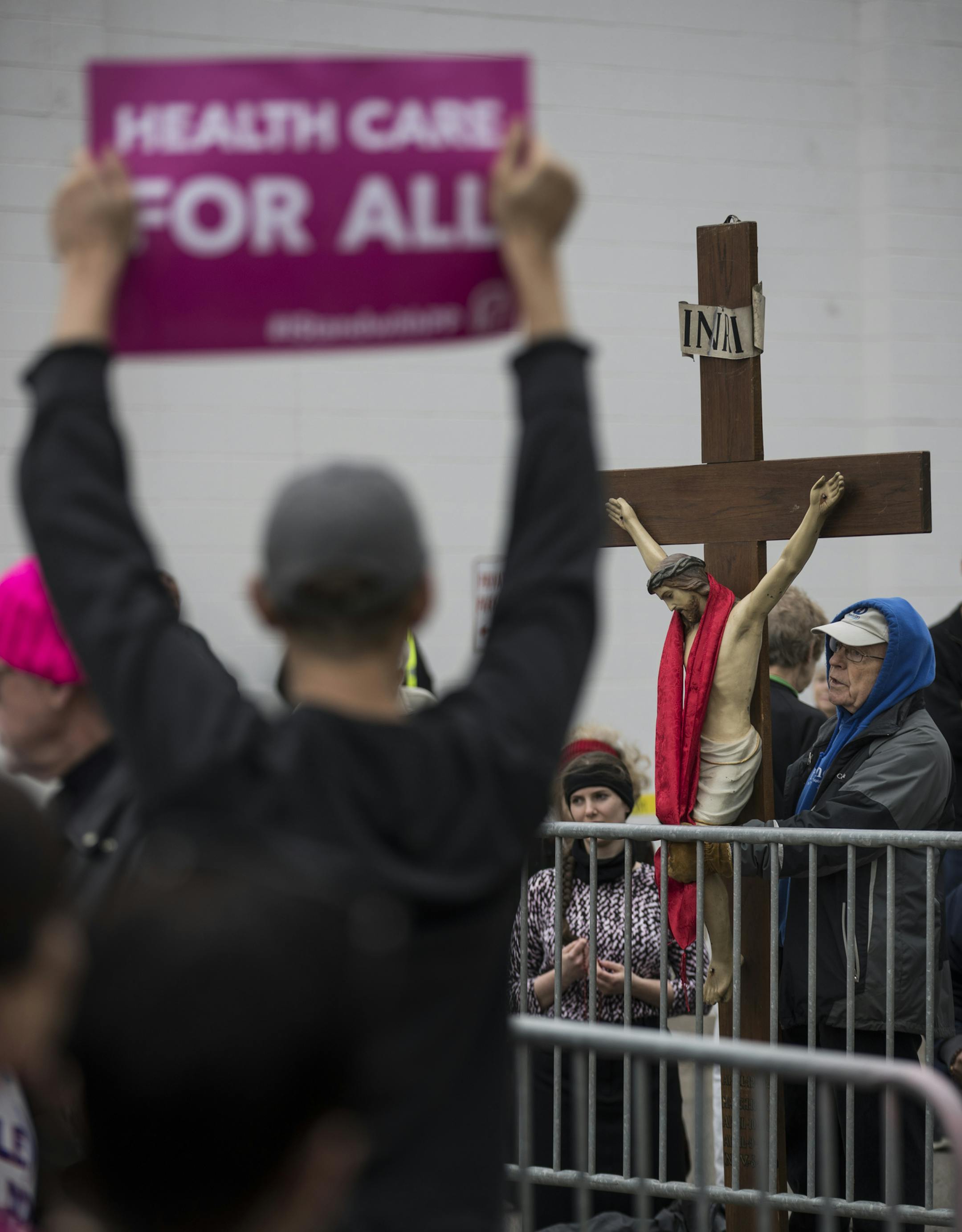 John Janzem held a cross he brought from Sacred Hearts in Robbinsdale as he stood on the pro-life side of a protest outside Planned Parenthood in St. Paul, Minn., on April 14, 2017. In the foreground at left are pro-choice marchers with signs supporting Planned Parenthood. ] RENEE JONES SCHNEIDER • renee.jones@startribune.com