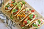 Hot dogs topped with a variety of toppings on a board for a summer gathering.