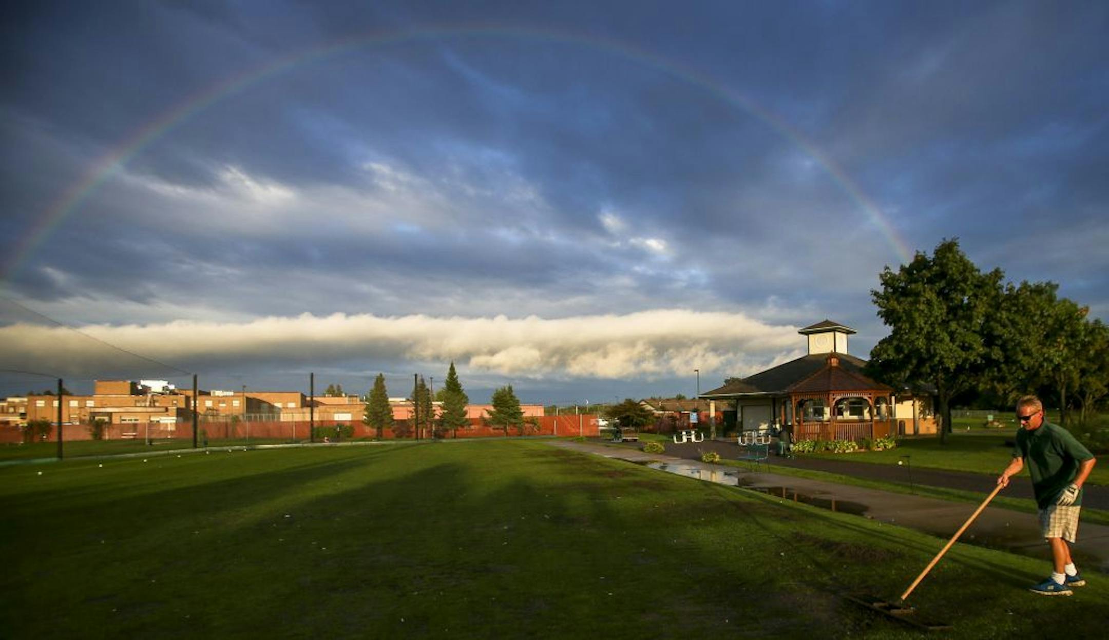 A light rainbow appears over the Hennepin County Department of Community Corrections and Rehabilitation as golf course porter Joshua Ulmsted resurfaces driving range tee boxes.
