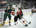 Calgary Flames defenseman Michael Stone (26) leaned into Minnesota Wild defenseman Jared Spurgeon (46) while they fought for control of a puck along t