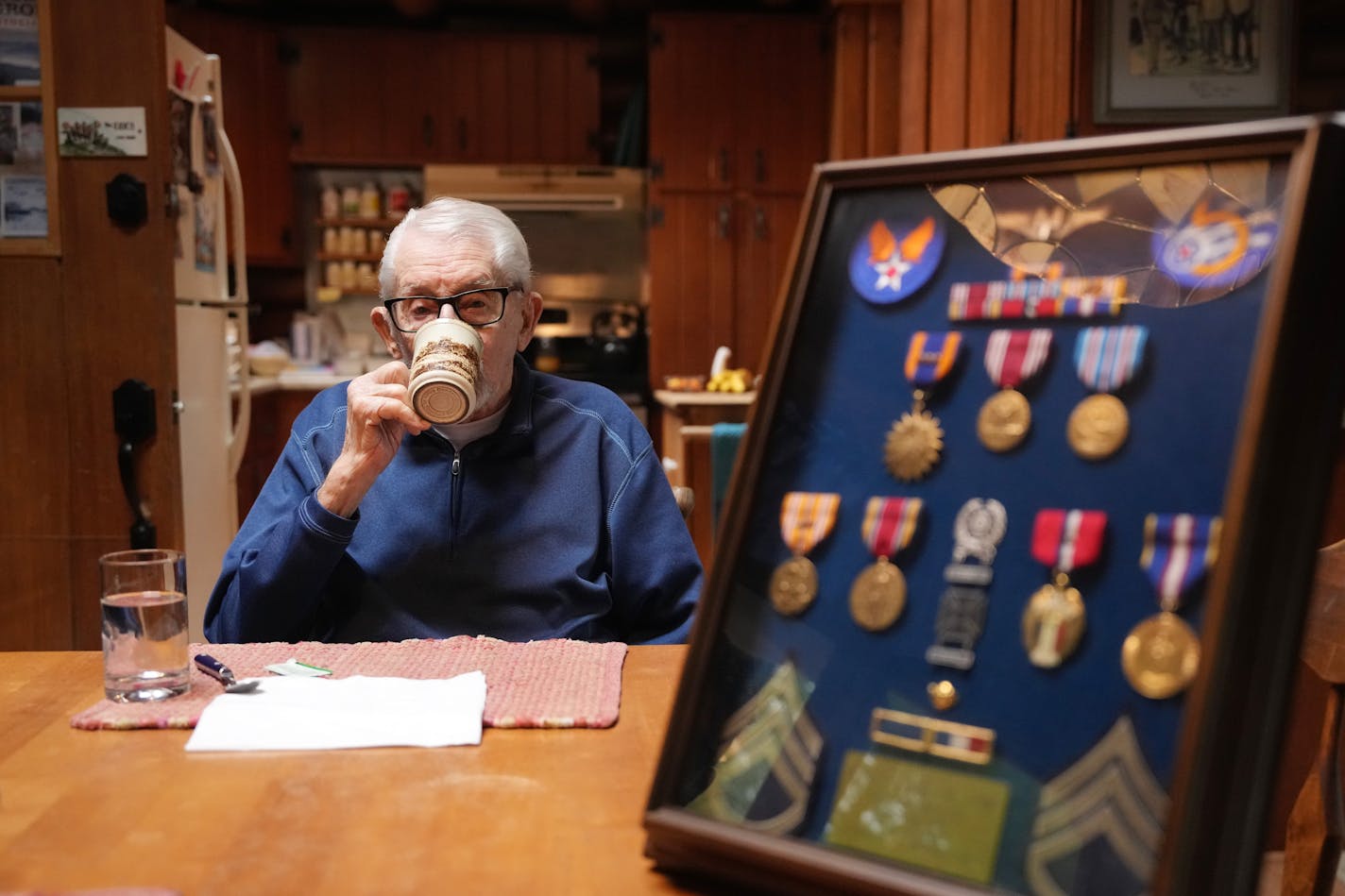 Jim Eide, a 100-year-old World War II veteran who served as a turret gunner, sipped his coffee as his daughter Vee Calder displayed his medals Wednesday in Longville, Minn.