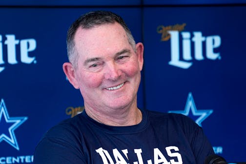 Close photo of Mike Zimmer in dark blue Dallas T-shirt against blue backdrop with "Lite" and Cowboys stars.