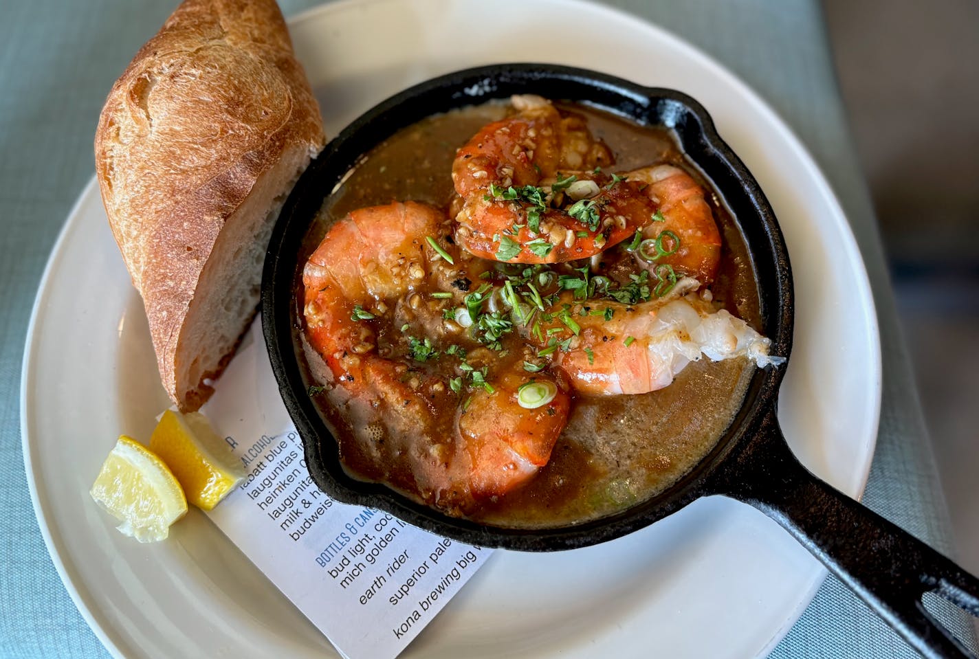 A cast iron pan with four giant shrimp in a butter and Worcestershire saunce on a plate with a hunk of baguette on the side.