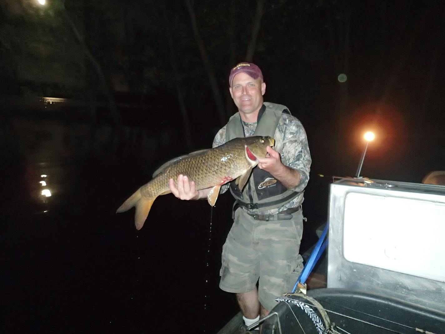 Beneath a full moon, bowfisherman Mark Ellenberg holds a common carp he shot with his bow last week on the St. Croix near where the Department of Natural Resources and anglers caught five invasive bighead carp. The invasive Asian carp were seven miles farther north in the St. Croix than they had been caught before.