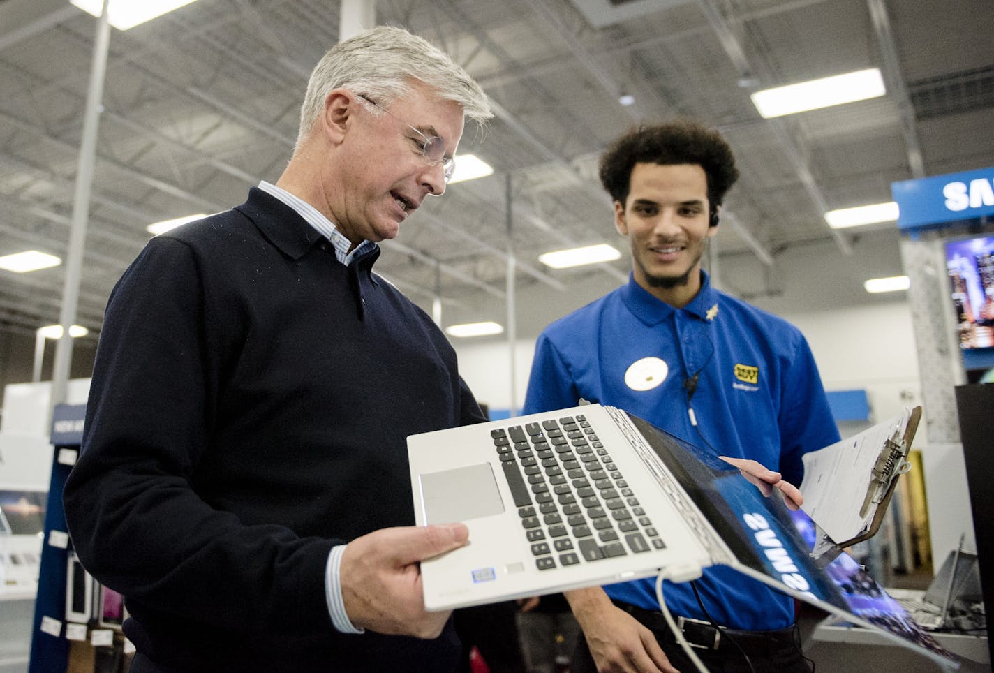 Best Buy CEO Hubert Joly examines a convertible laptop on the sales floor with sales representative Justus Murphy.