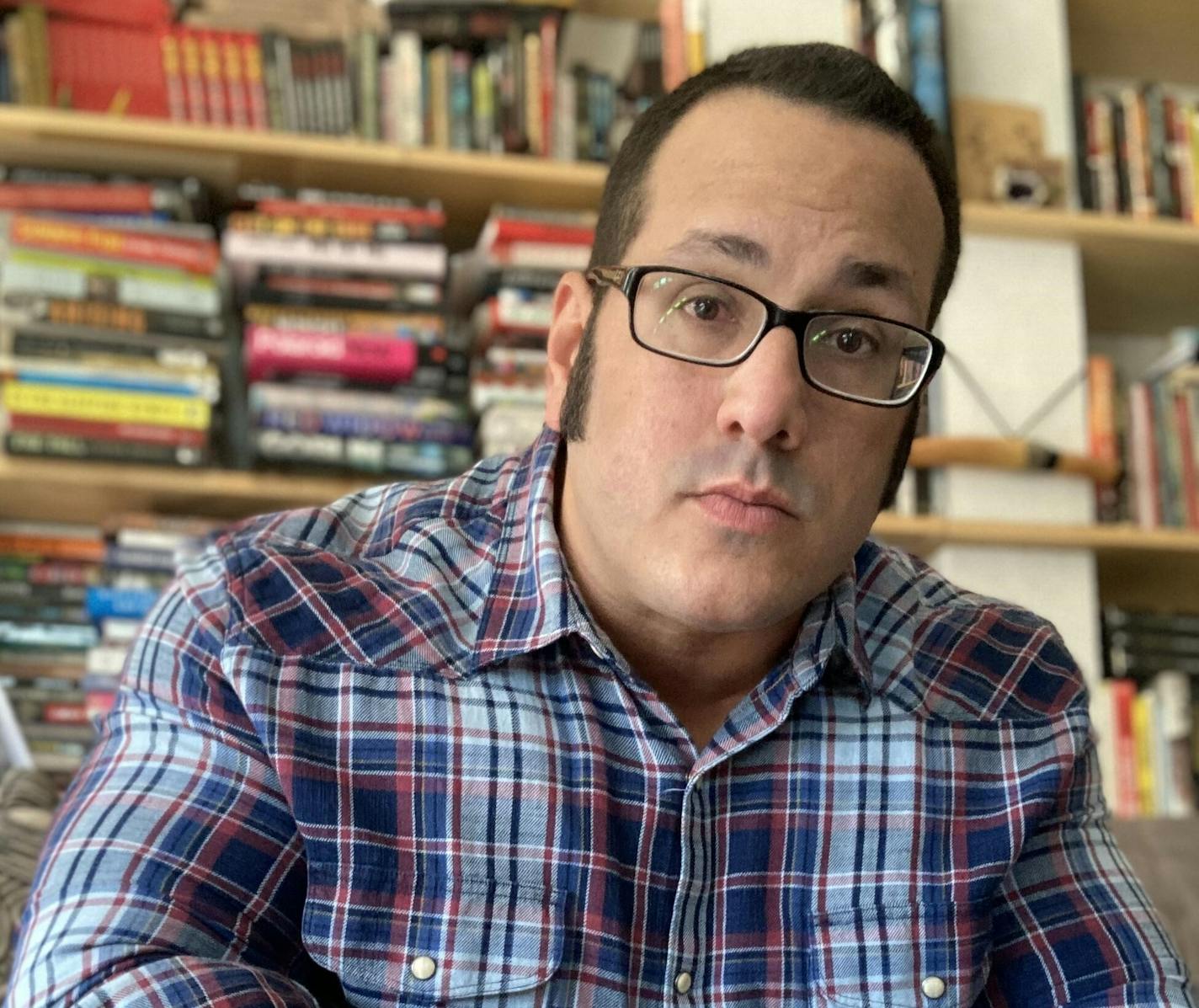 photo of author Gabino Iglesias in front of a bookshelf