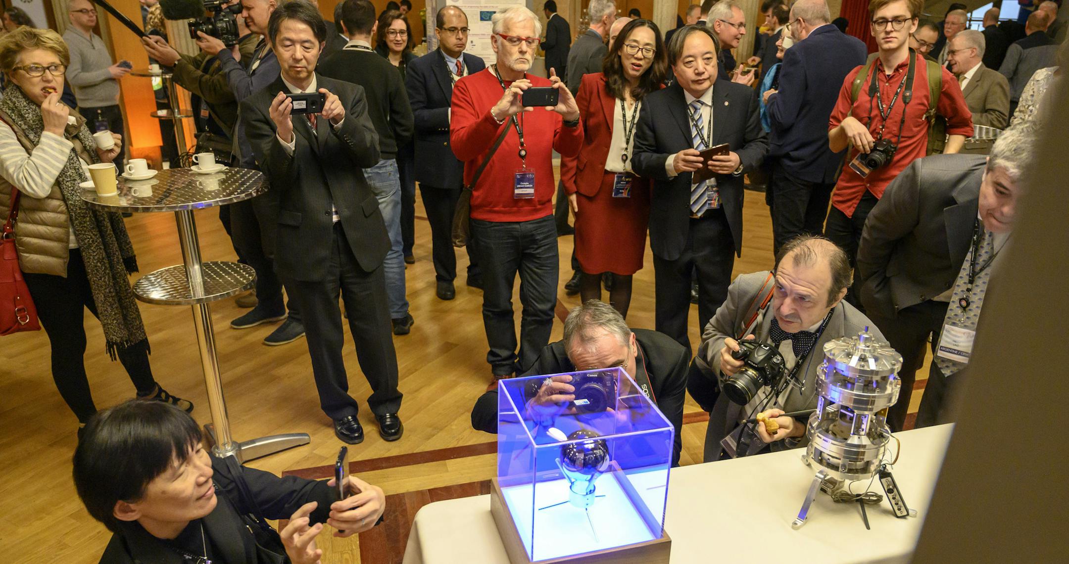 Attendees photograph a silicon-crystal sphere, left, and a Kibble balance at the General Conference on Weights and Measures in Versailles, France, Nov. 16, 2018. International scientists voted unanimously here to redefine the kilogram and three other basic units of measurement: the, the mole, the kelvin, and the ampere. (Matt Roth/The New York Times)