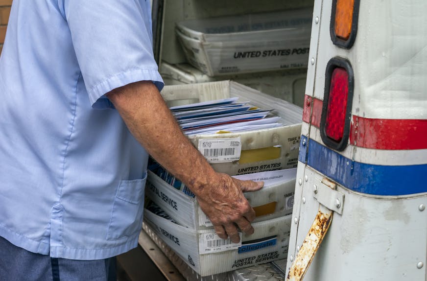 Letter carriers load mail trucks for deliveries at a U.S. Postal Service facility in McLean, Va., Friday, July 31, 2020. Delays caused by an increase in voting by mail may contribute to public doubts about the results. The public might not know the winner of the presidential race on Election Day because of a massive shift to voting by mail during the coronavirus pandemic. That's because mail ballots take longer to count because of security procedures and laws in some states that limit when they