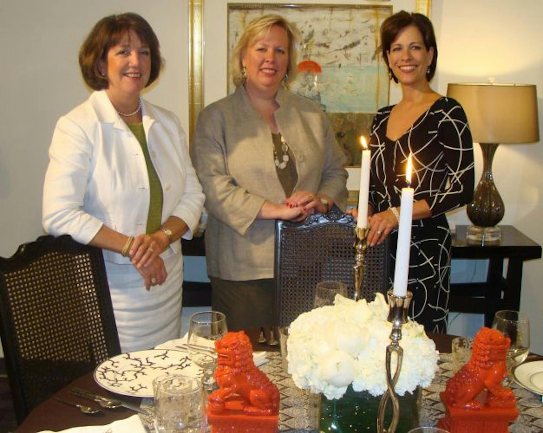 Talla Skogmo, Linda Engler and Renee LeJeune Hallberg, all with Engler Skogmo Interior Design, posing next to their table setting. It features dishes donated by JB Hudson.