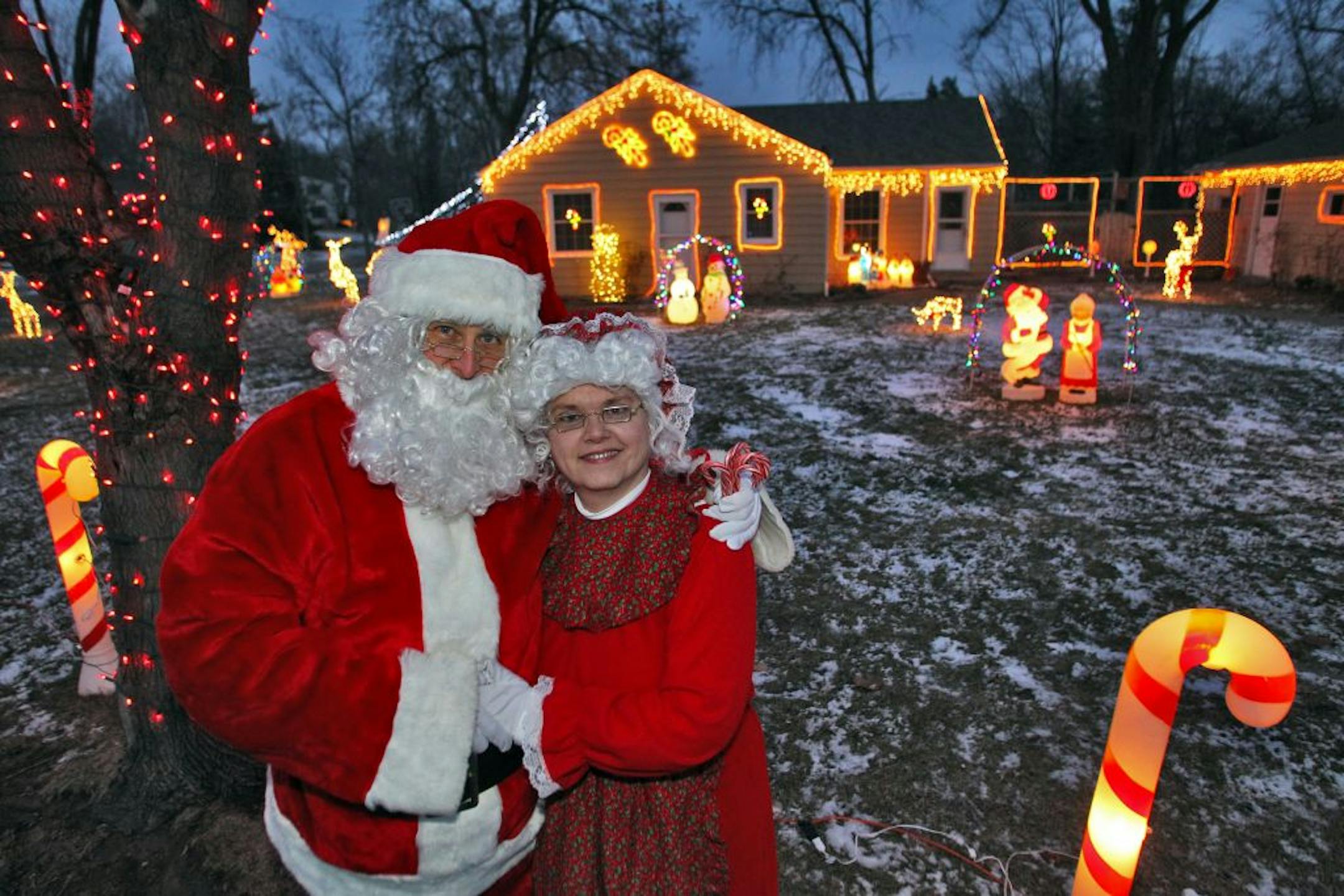 Richard and Lynn Rozell, dressed as Santa and Mrs. Claus, stood in their Hopkins yard with holiday lights in the background.
