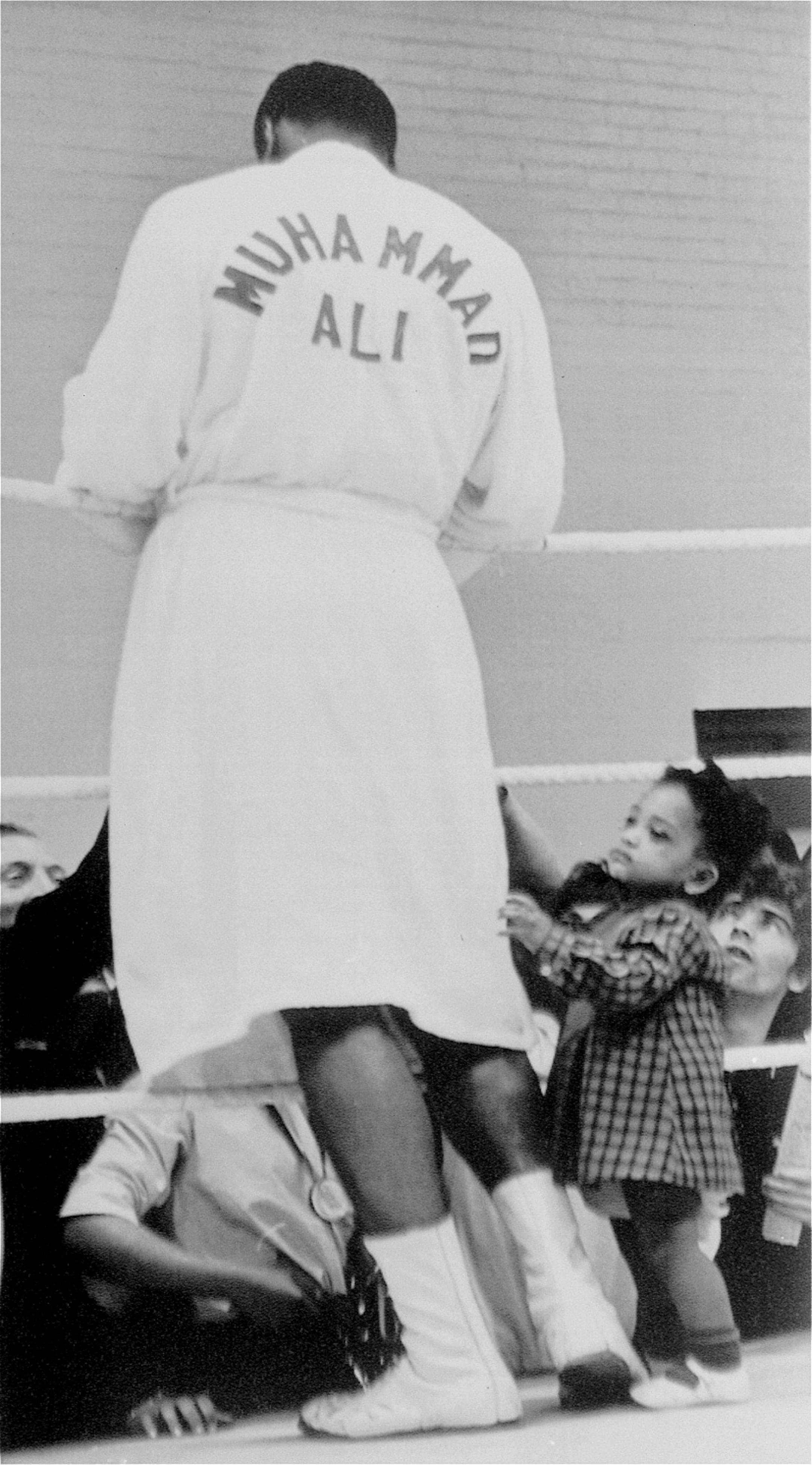 Two year old Shelley Obermuller tugs for the attention of Muhammad Ali as the world heavyweight champion gives autographs to admirers during a training session in London, England, May 17, 1966. Ali will defend his title against British heavyweight king Henry Cooper when they meet in the British capital in a title bout May 21.
