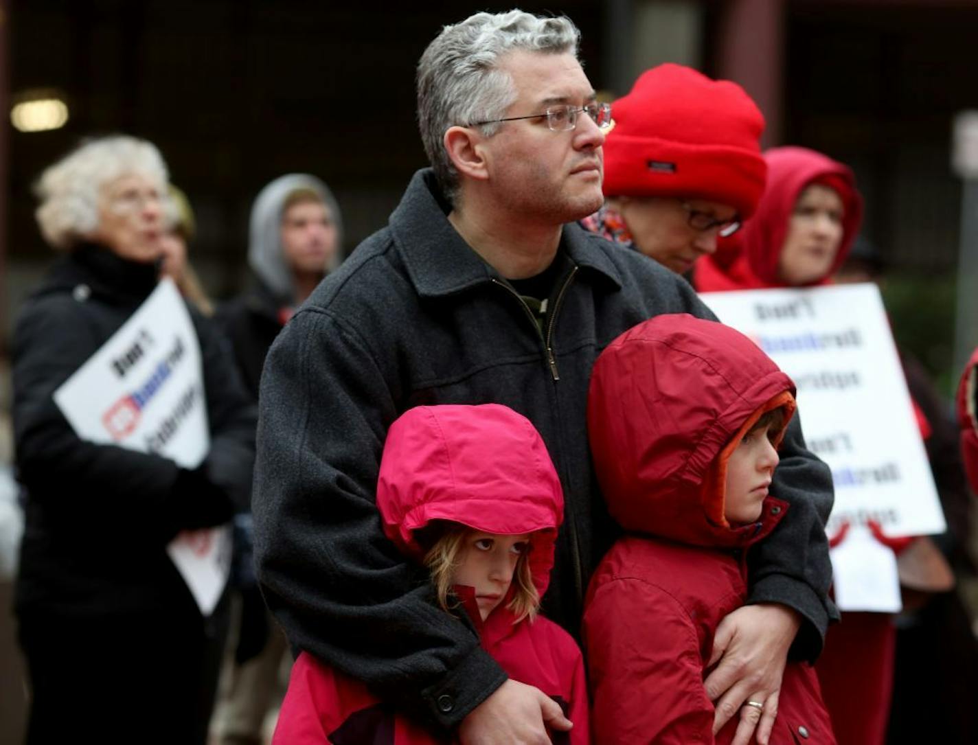 Dave Snyder, with his children Nora, 6, Spencer, 8, listen as Tony Frank and Travis Decory open the climate change march with some traditional drumming and singing at the Hennepin County Government Center.
