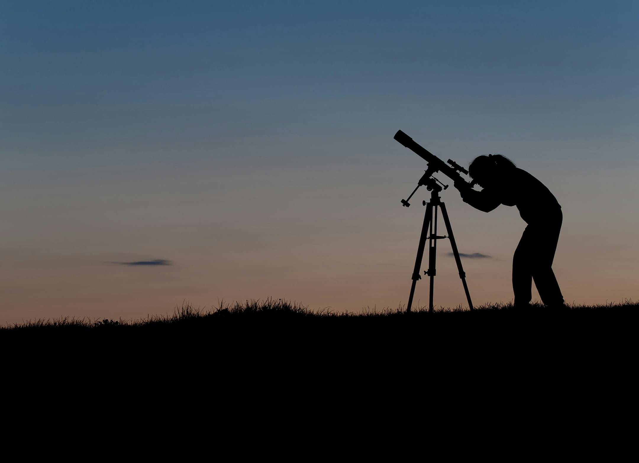 Female amateur astronomer observing the night sky using a three inch refracting telescope on an equatorial mount.