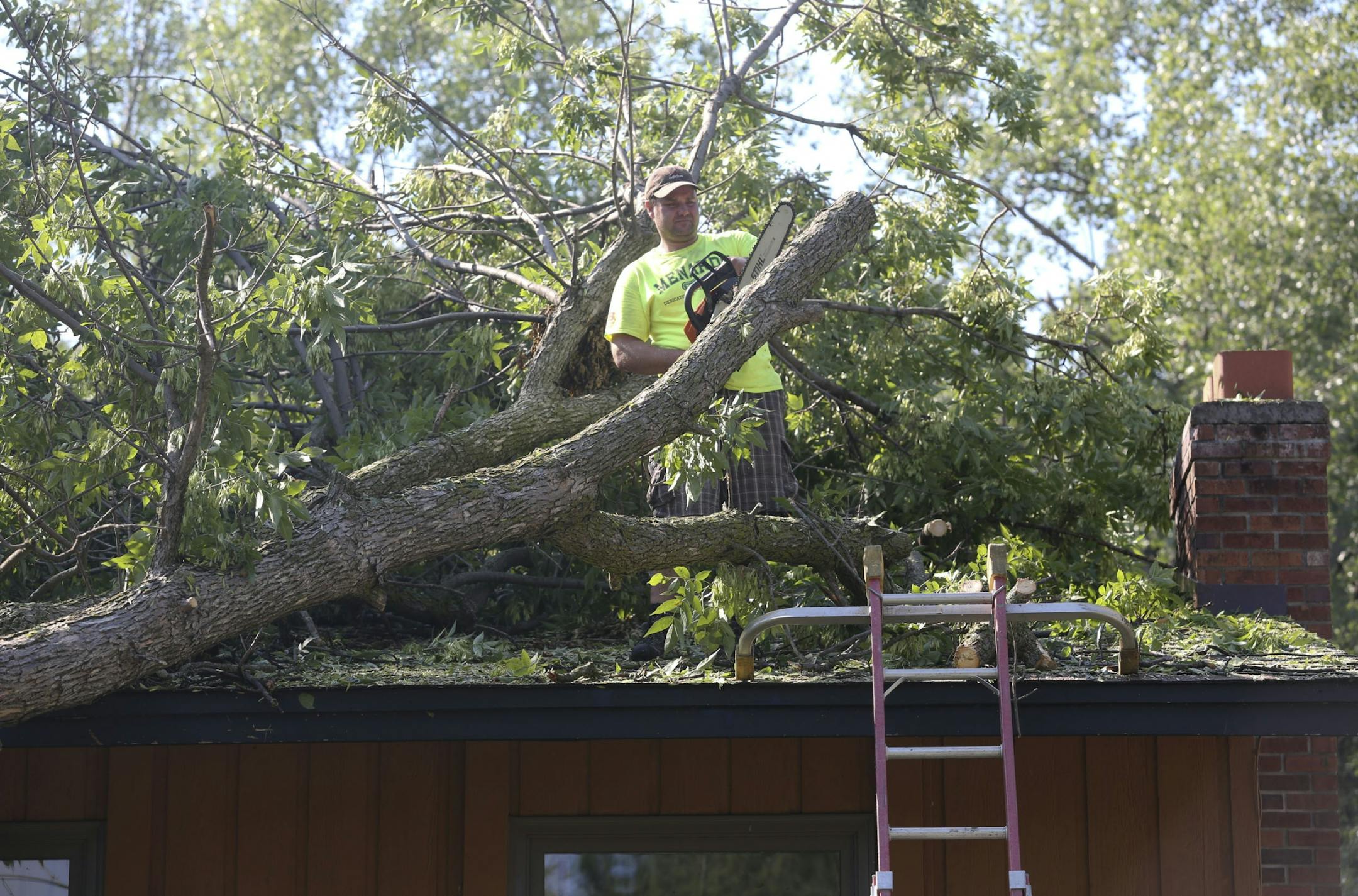 Jason Berg worked on cutting branches of a tree that fell on his neighbor Bill Winter's house in Bloomington Park.
