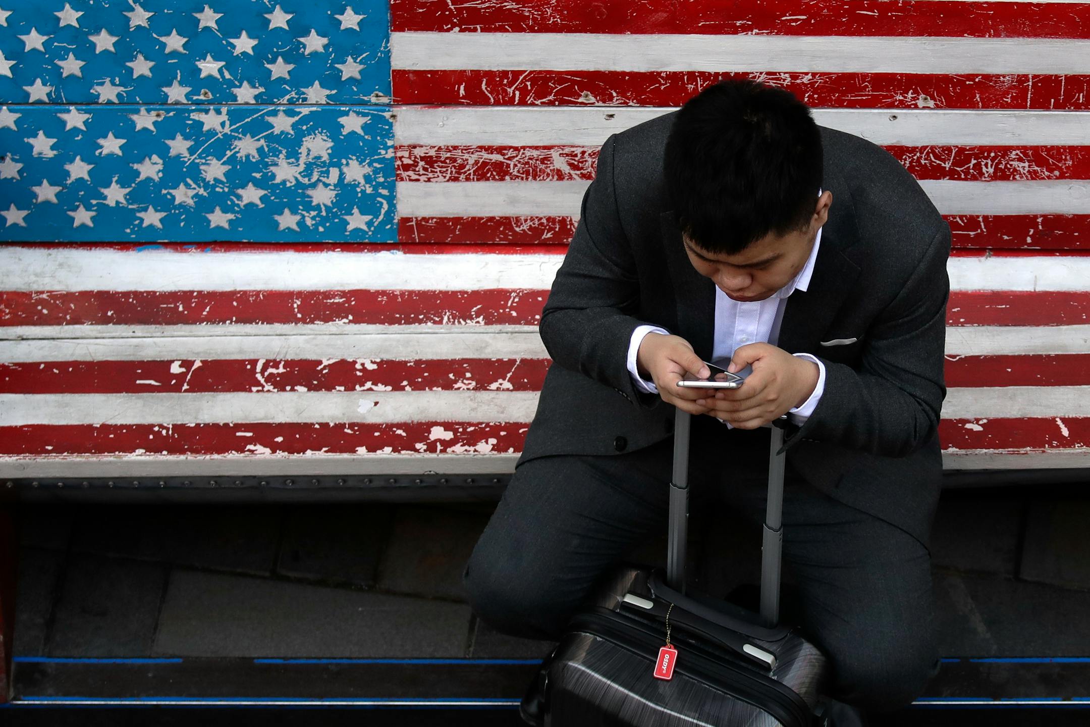 A man checked his smartphone while sitting on an American flag bench.