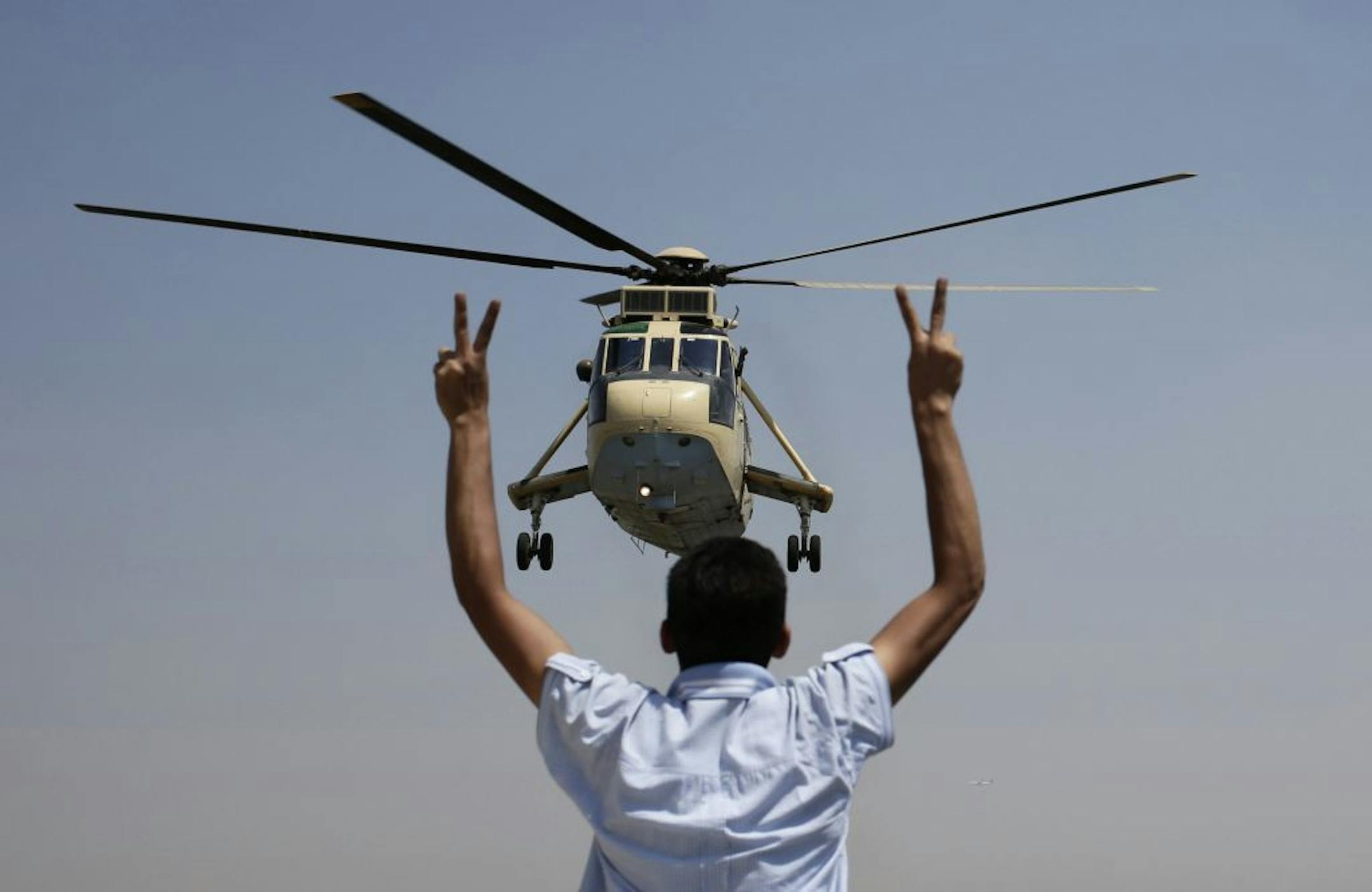 A man flashes victory signs at an Egyptian military helicopter as it flies over the presidential palace in Cairo, Egypt, Friday, July 26, 2013.