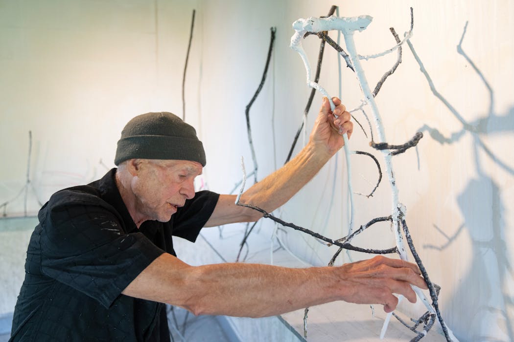 At his farm studio, Russell Sharon handles one of his branch sculptures, which he calls “debutantes” for the way they resemble a group of dancers.