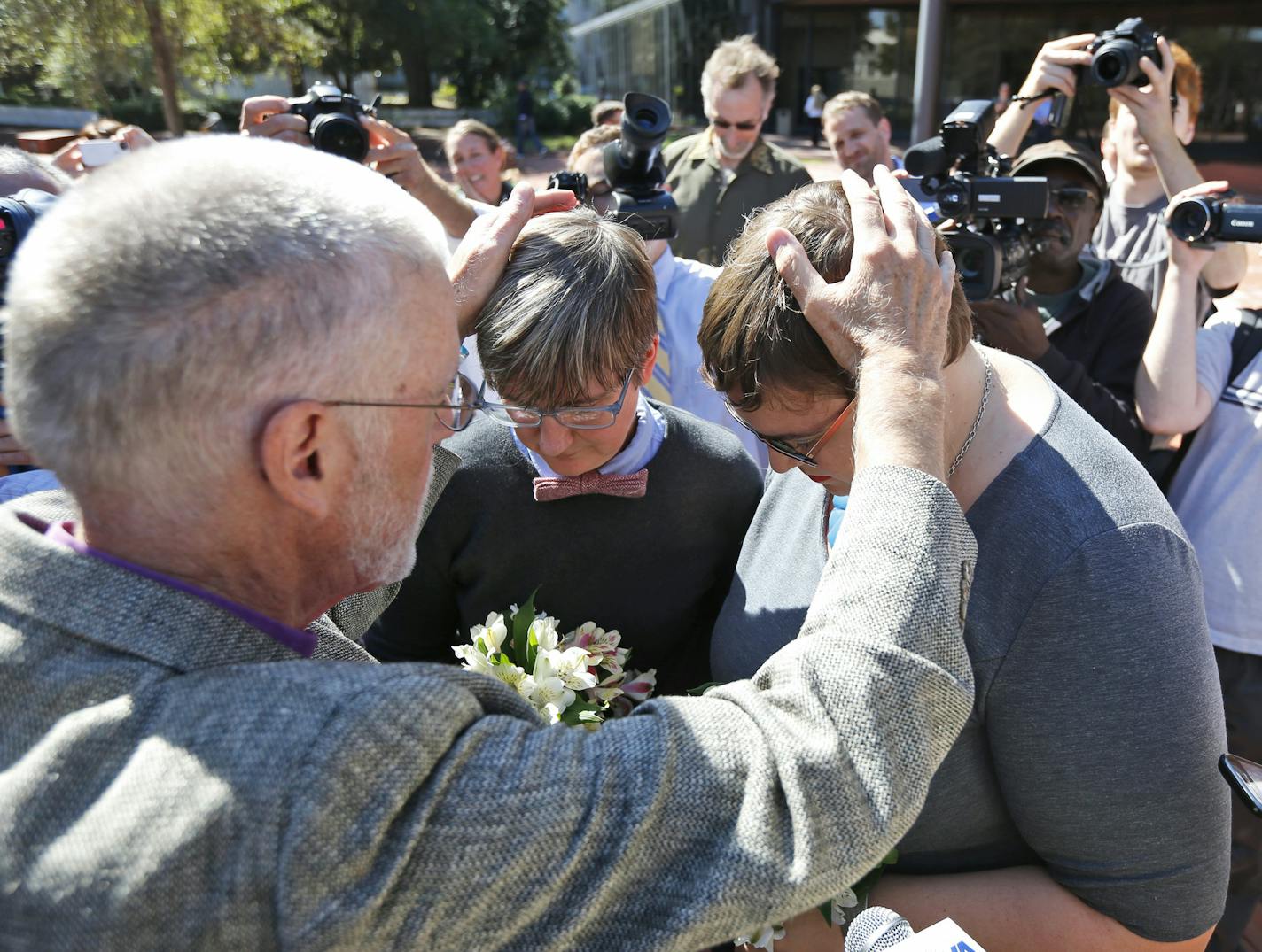 Rev. Robin Gorsline, left, marries Nicole Pries, center and Lindsey Oliver, one of the first same-sex couples in Virginia to be married, Monday, Oct. 6, 2014, outside a Richmond Court building in Richmond, Va. The couple were the first in the Richmond are to be married after the U.S. Supreme Court refused to overturn same-sex marriage prohibitions. (AP Photo/Steve Helber)