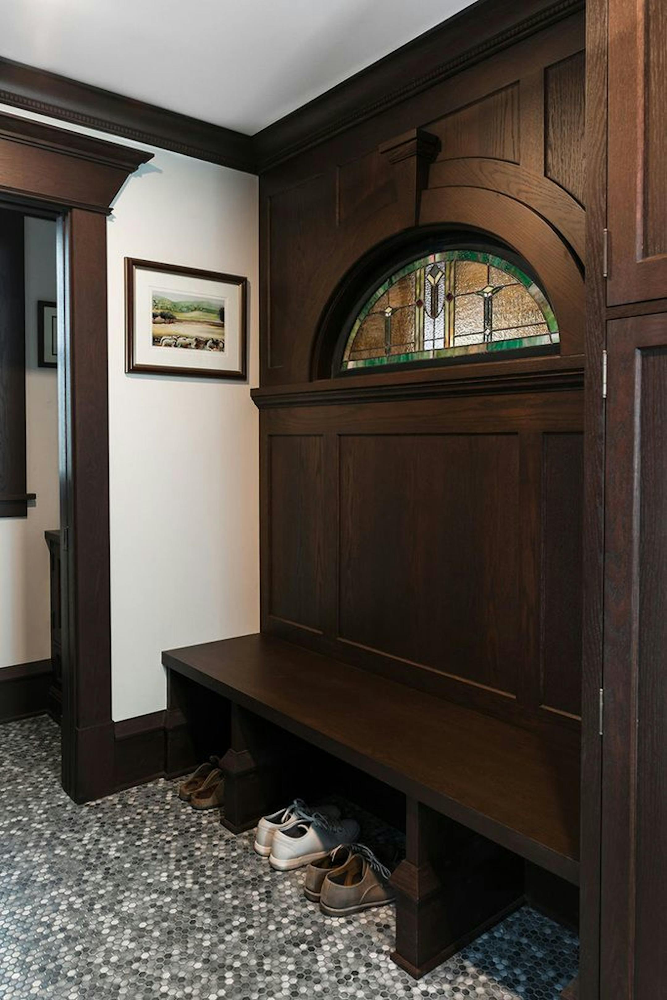 The mudroom features a built-in bench that incorporates the stained-glass window in the built-in buffet on the wall behind the bench.