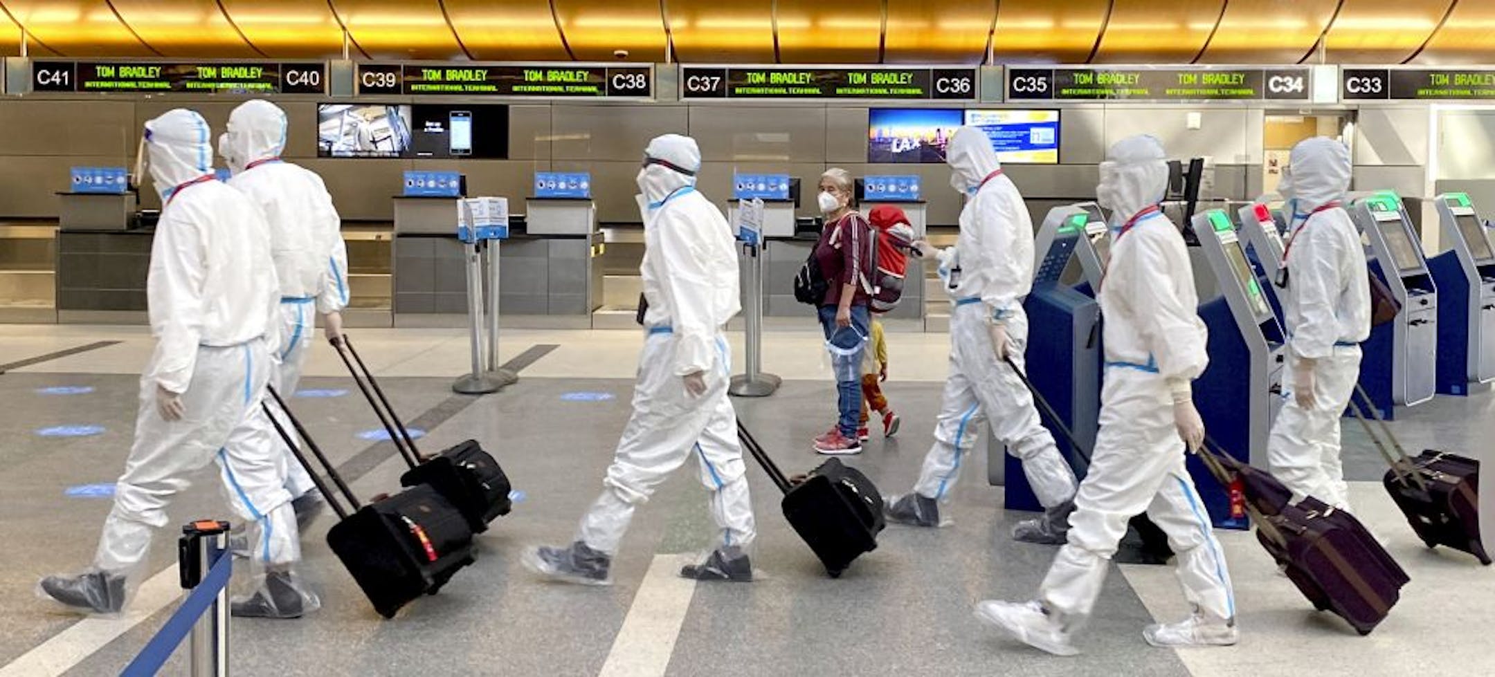 A woman, accompanied by a child, looks over as an airline crew wearing full personal protective equipment against COVID-19 walks through the international terminal at Los Angeles International Airport in Los Angeles on Tuesday, Nov. 17, 2020.