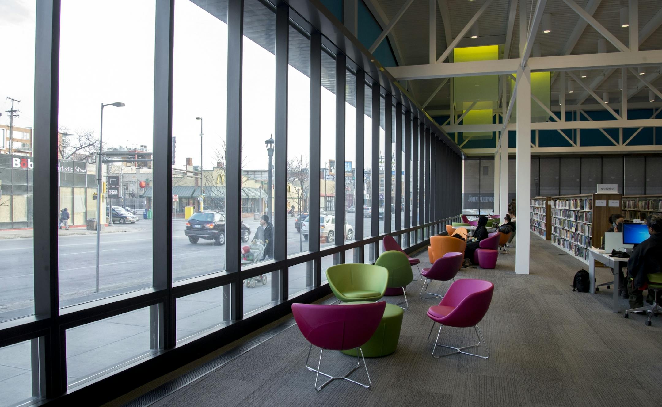Visitors read in colorful chairs at Walker Library, as pedestrians walk past outside.