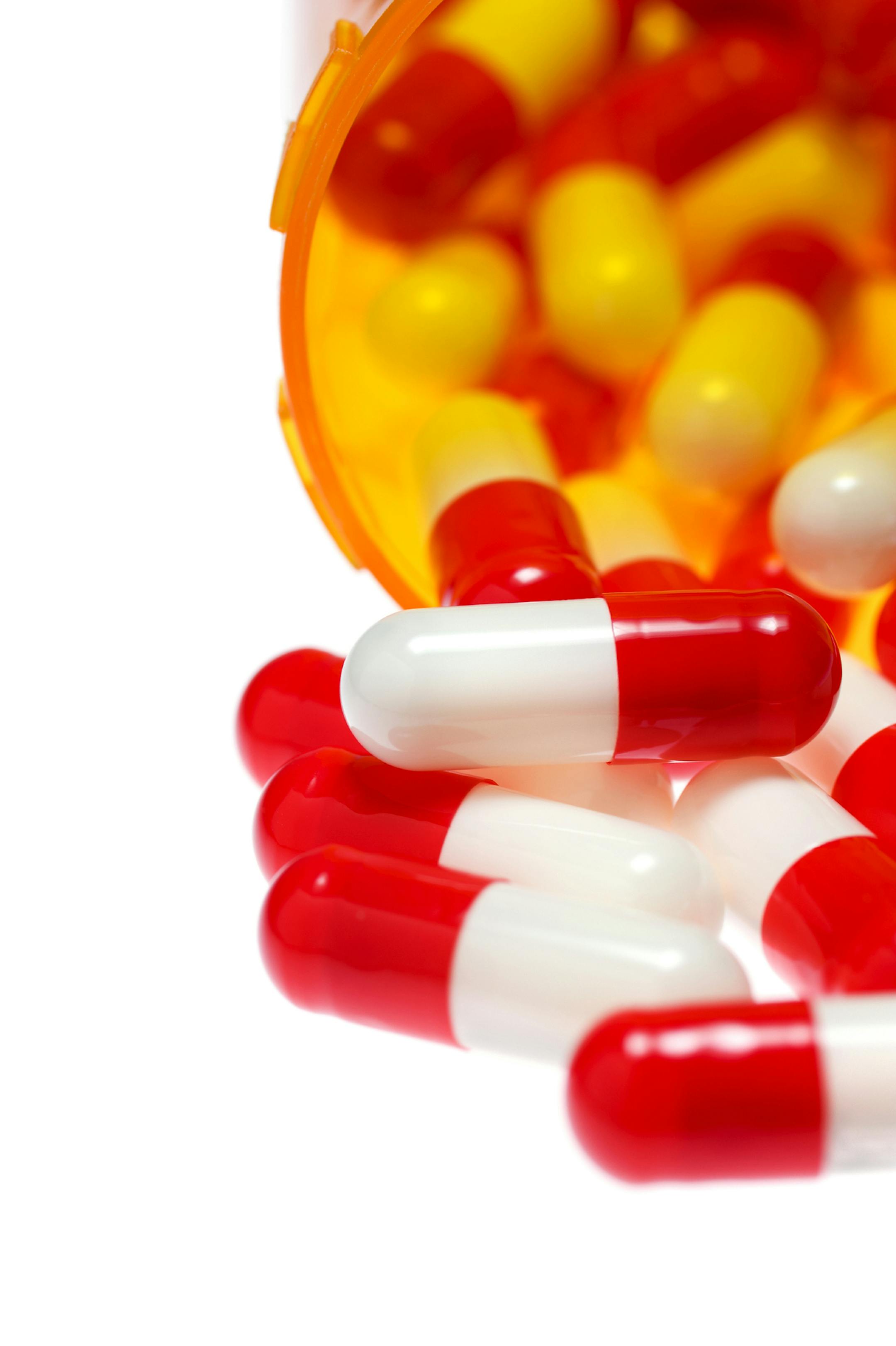 An amber pill bottle with blue and white capsules pouring out on a white background with various colored capsules in pill bottles behind ORG XMIT: 12_MED