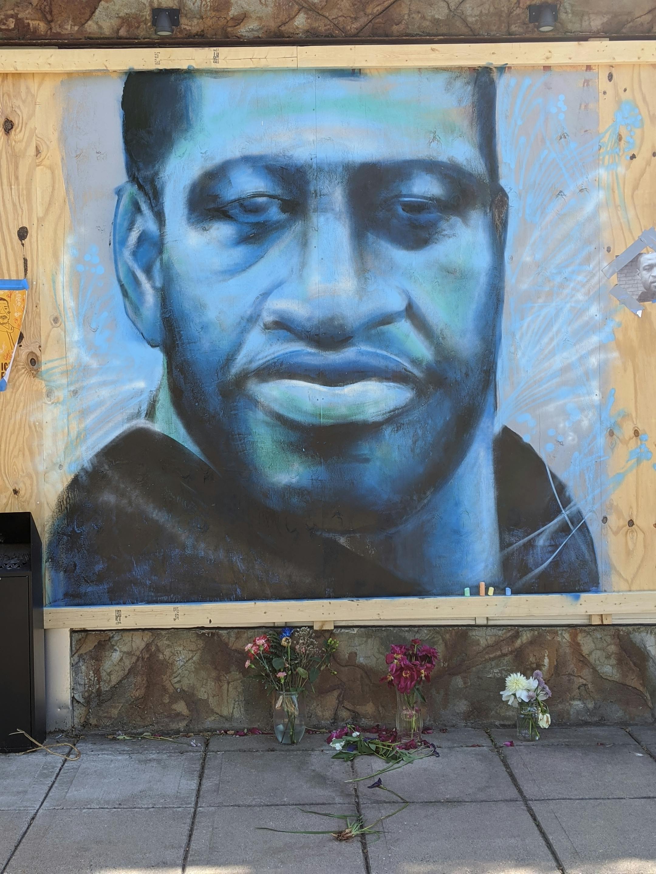 A blue-tinted version of a stoic, strong-looking George Floyd covers the boarded-up door of Leviticus Tattoo and Body Piercing at 4109 E Lake St.