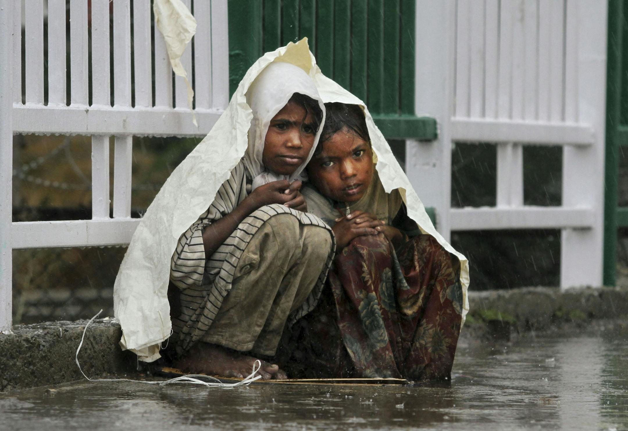 Children use a plastic sheet to take shelter from rain in Srinagar, India, Friday, Aug.12, 2011.