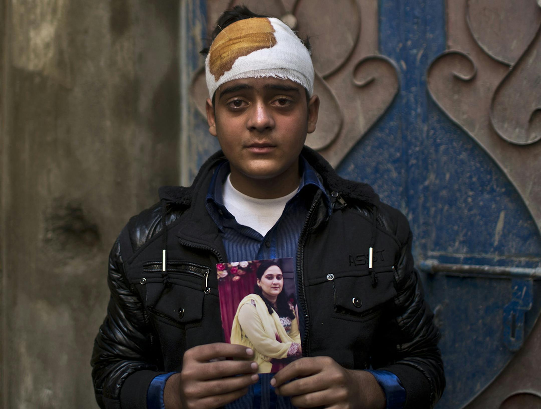 Pakistani student, Mohammad Baqair, who survived last Tuesday's Taliban attack on a military-run school and was slightly injured, poses for a picture holding a photograph of his mother a victim of the attack, who was a teacher at the school, at his home, in Peshawar, Pakistan, Thursday, Dec. 18, 2014. The Taliban massacre that killed more than 140 people, mostly children, at a military-run school in northwestern Pakistan left a scene of heart-wrenching devastation, pools of blood and young lives