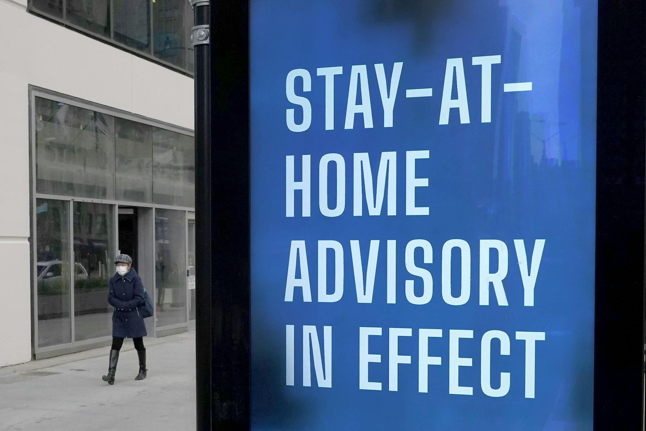 FILE - In this Nov. 18, 2020, file photo, a lone pedestrian walks past a public service sign reminding Chicago residents of the return to a stricter COVID-19 protocol along the city's usually busy Magnificent Mile in Chicago. With the coronavirus surging out of control, the nation's top public health agency advised Americans on Thursday, Nov. 19, not to travel for Thanksgiving and not to spend the holiday with people from outside their household. (AP Photo/Charles Rex Arbogast, File)