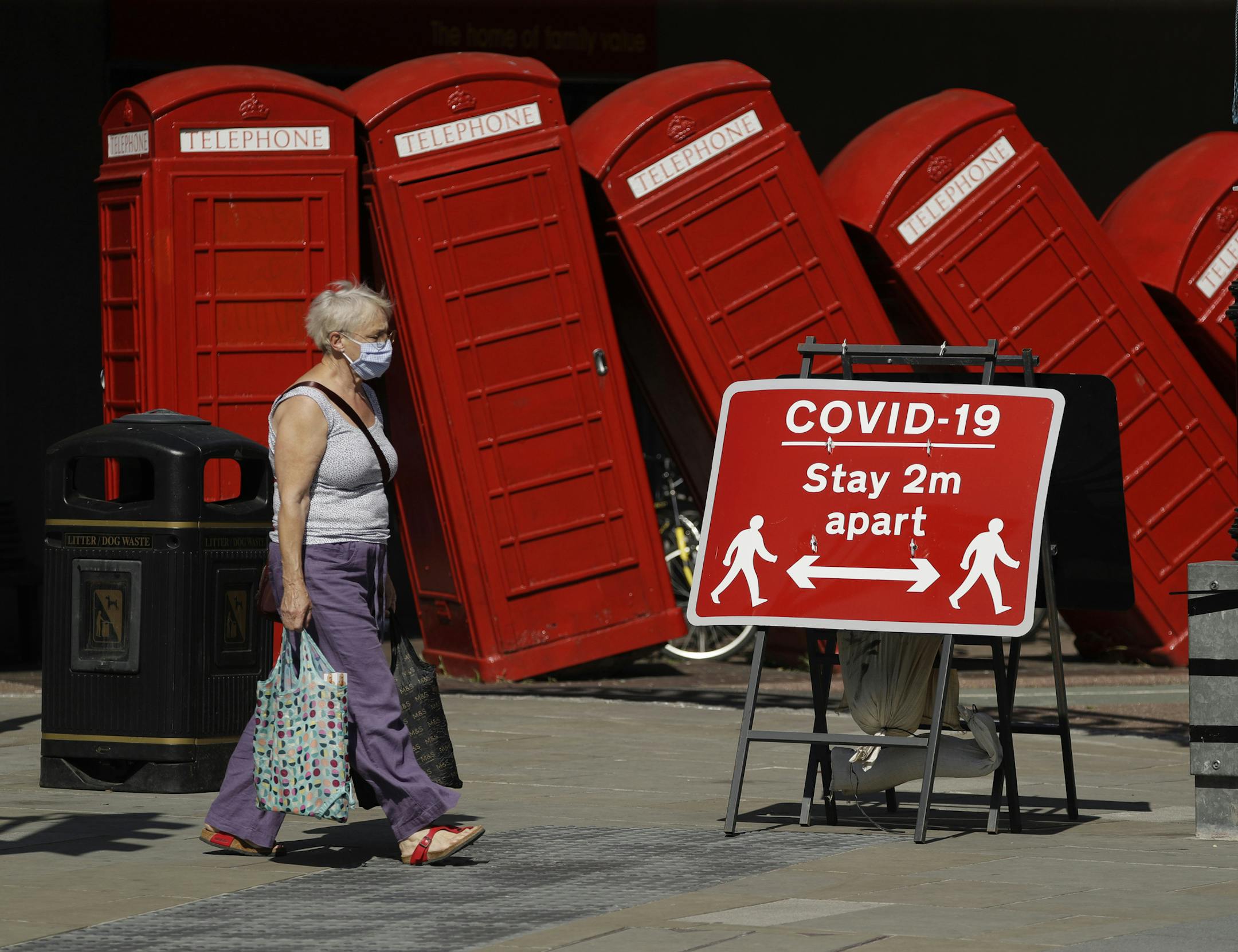 FILE - In this file photo dated Monday, June 22, 2020, a sign requesting people stay two metres apart to try to reduce the spread of COVID-19 is displayed in front of "Out of Order" a 1989 red phone box sculpture by British artist David Mach, in London. The British government insists that science is guiding its decisions as the country navigates its way through the coronavirus pandemic. But a self-appointed group of independent experts led by a former government chief adviser says it sees little