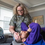 Kathy Ware calms son Kylen, 29, as he is secured to a stander as part of his physical therapy at their South St. Paul home. The stander helps Kylen, w