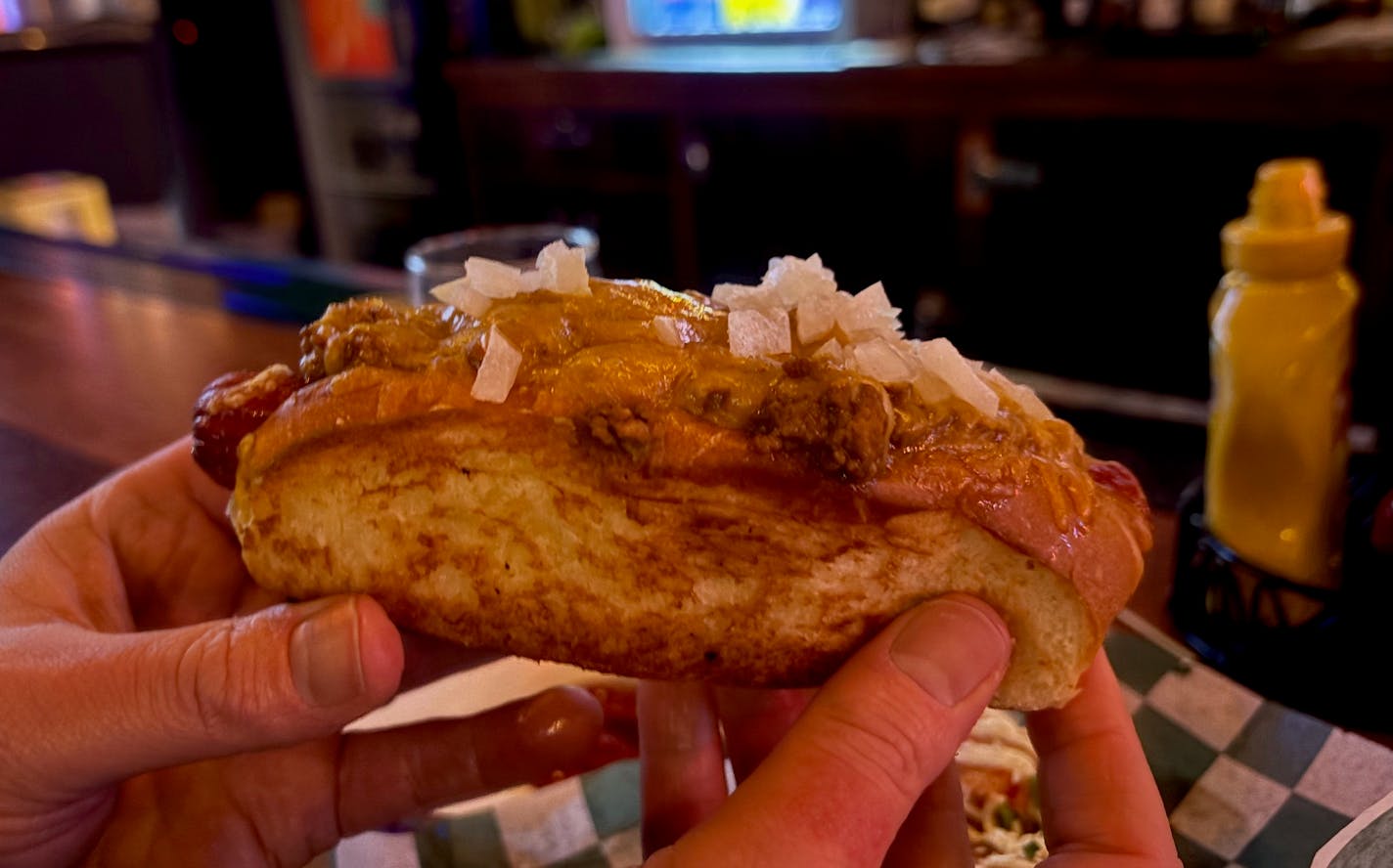 A toasted bun holding a hot dog topped wth coney meat, cheese and raw onions.