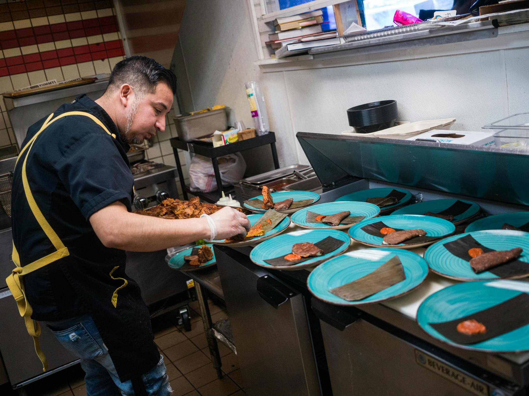 Chef Cristian de Leon plates lamb birria in the crowded kitchen.