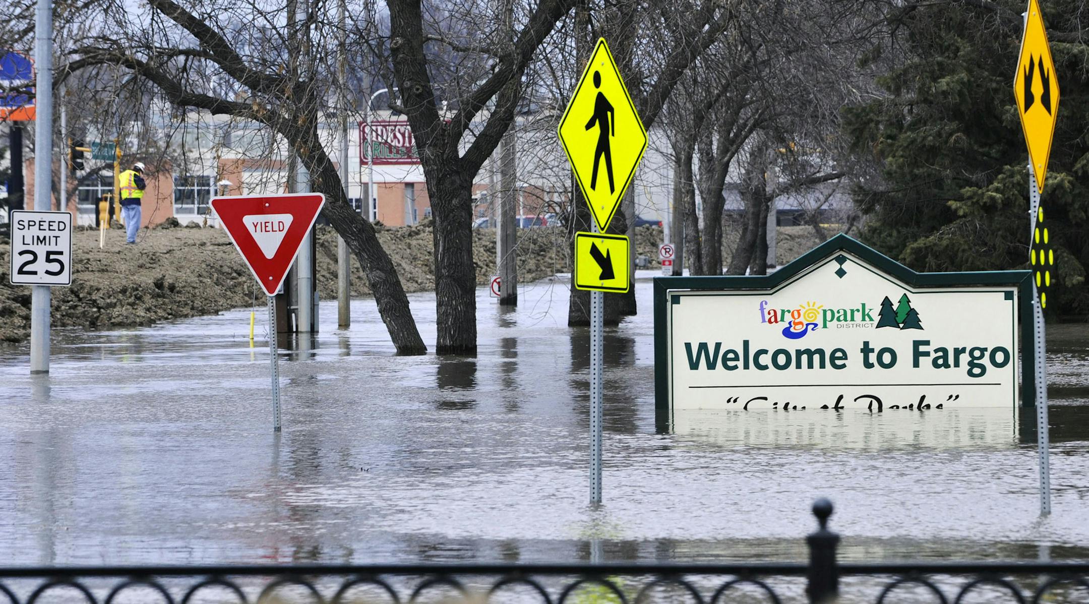 FILE - In this April 8, 2011 file photo, a welcome sign for Fargo, N.D., sits in the rising floodwaters of the Red River as a flood engineer for the U.S. Army Corps of Engineers, at left, inspects the levee protecting the downtown area. The decision by the Buffalo Red River Watershed District in Minnesota to back out of an agreement for a Red River diversion project around the Fargo area has raised questions about permits for the $2.1 billion channel. (AP Photo/Jim Mone, File) ORG XMIT: MIN20160