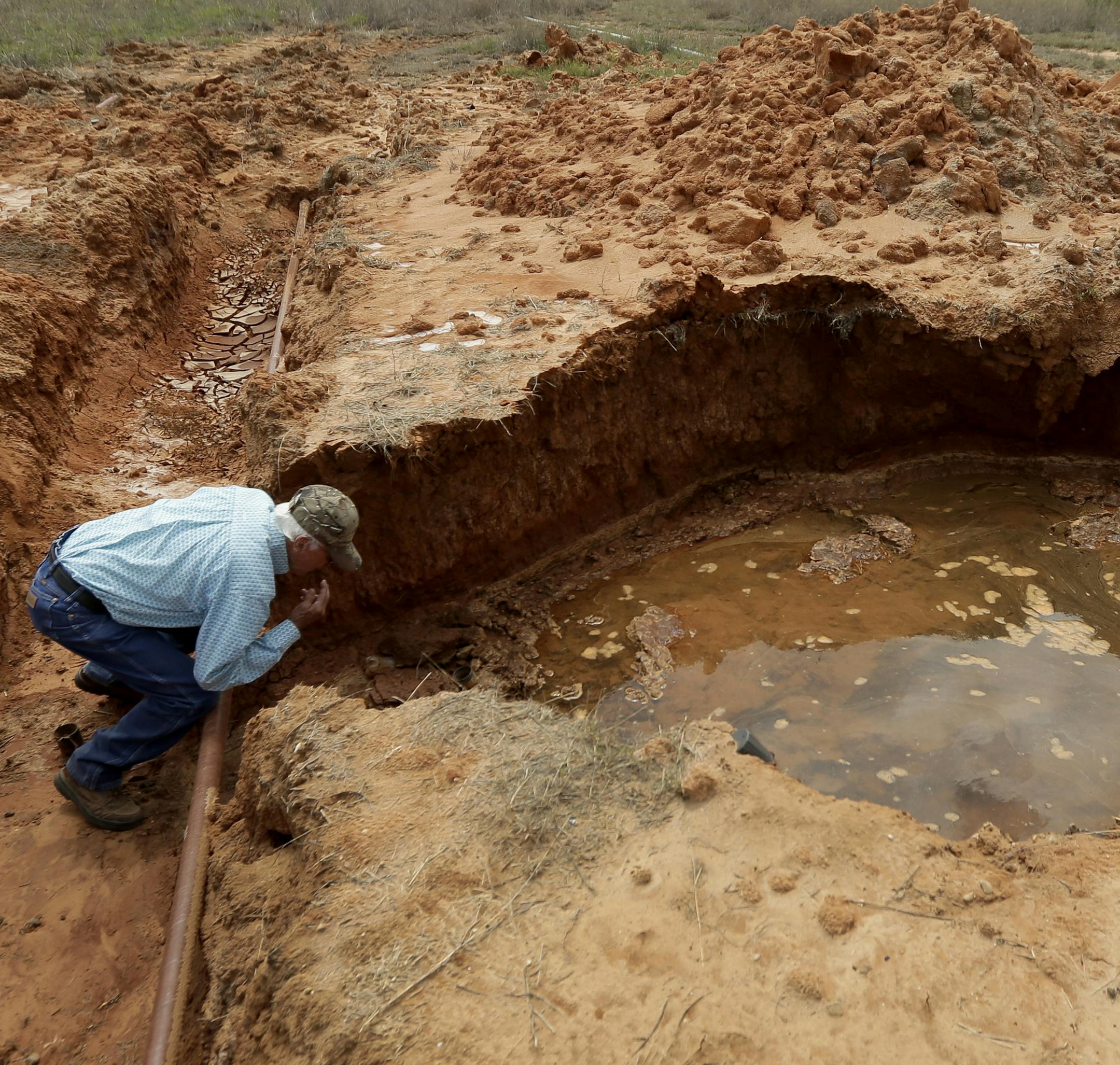 ADVANCE FOR USE TUESDAY, SEPT. 8, 2015 AND THEREAFTER - In this April 22, 2015 photo, Wesley Graves looks over a crater left after a saltwater disposal pipeline ruptured on his ranch near Snyder, Texas. Equipment failure is a major cause of oilfield wastewater spills. (AP Photo/Charlie Riedel)