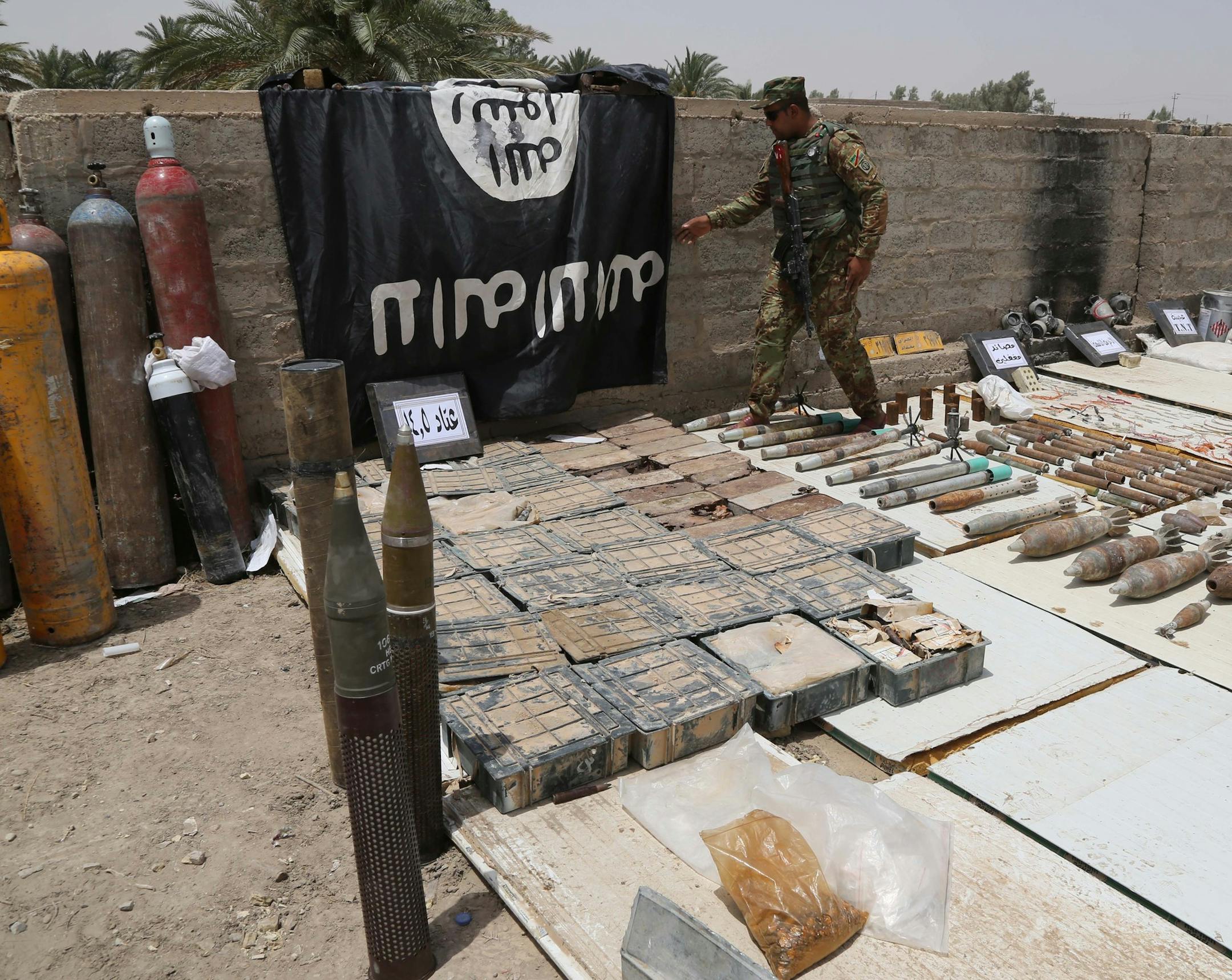 Iraqi security forces display a flag of the Islamic State group and weapons and ammunition confiscated after regaining control of during operations over the last week, from towns of al-Karma and Saqlawiyah near Fallujah, at al-Taji Camp north of Baghdad, Iraq, Friday, July 10, 2015. (AP Photo/ Karim Kadim)