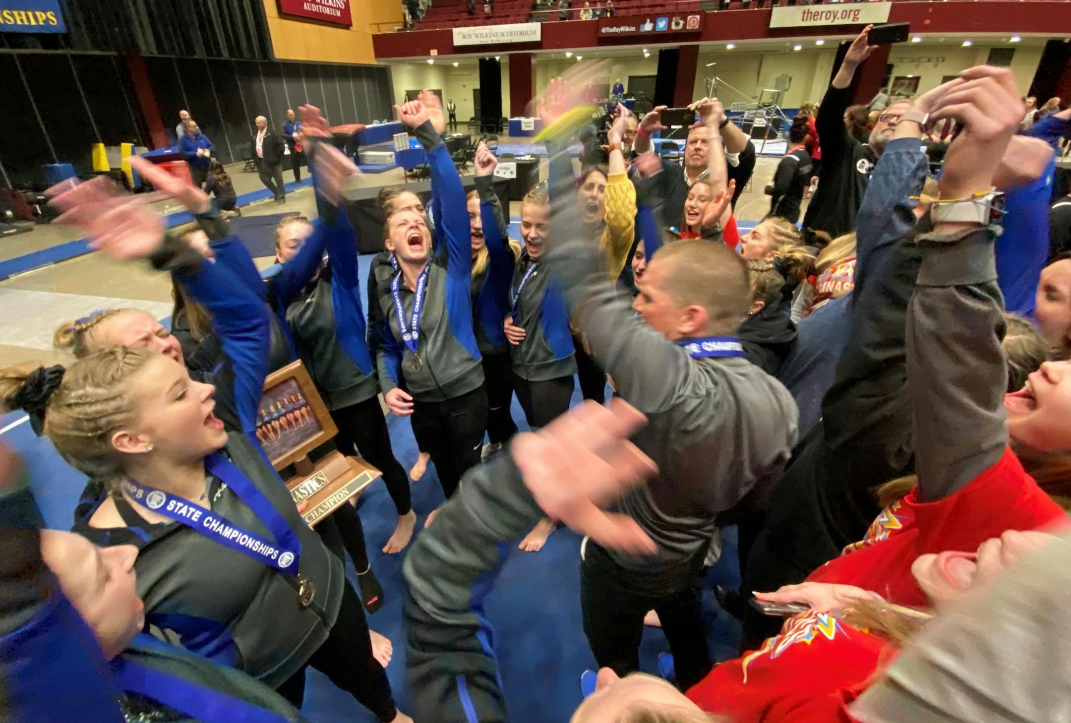 Big Lake gymnastics teammates celebrate with their Class 1A team championship trophy Friday at Roy Wilkins Auditorium in St. Paul. Photo courtesy Paul Krumrei