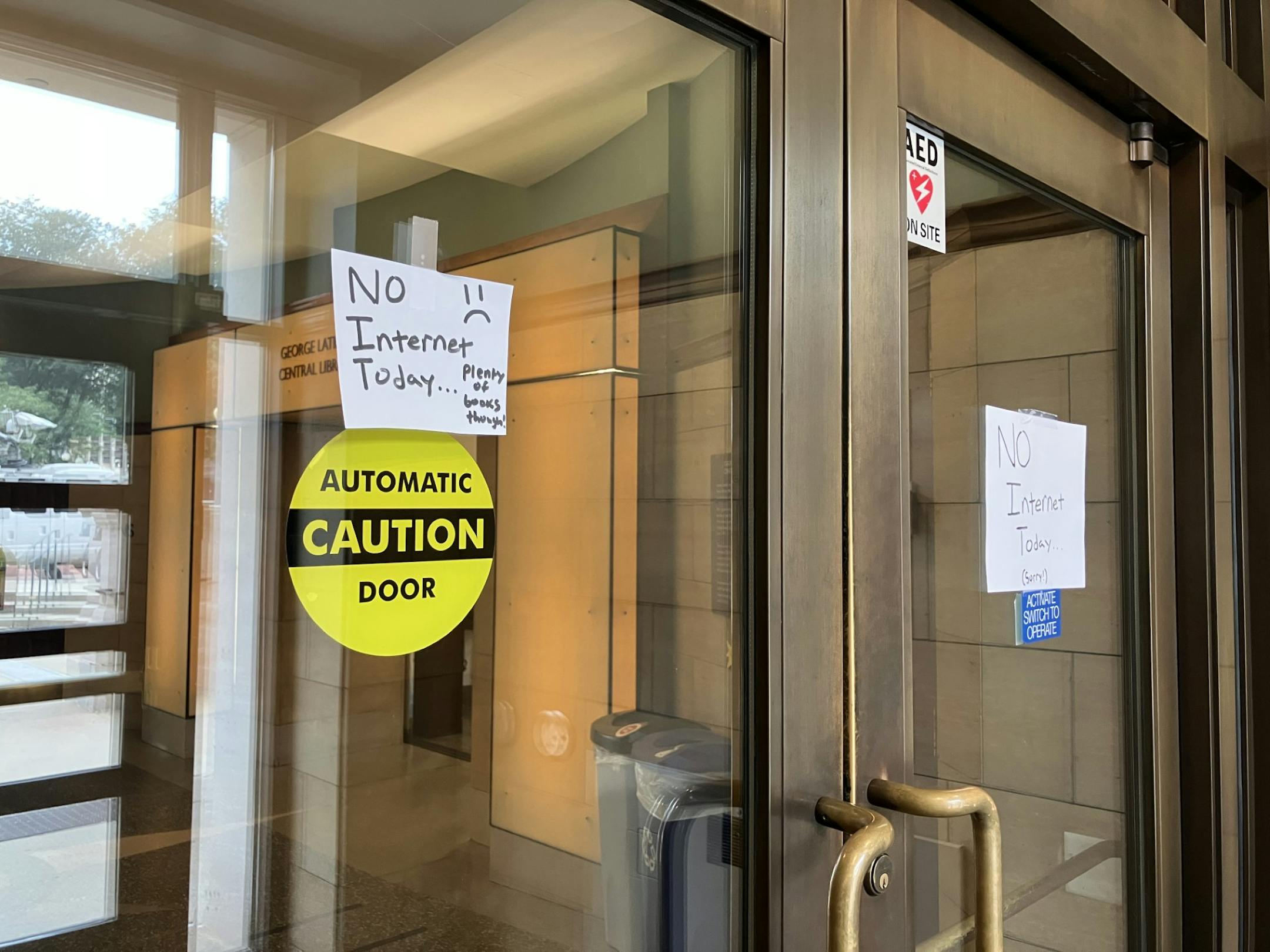A white paper sign taped to a glass door "No internet today" with a frowny-face. In smaller letters, the sign continues: "Plenty of books though."