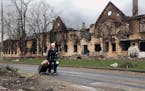 A woman pulls her bags past houses damaged during fighting in eastern Mariupol, Ukraine, Friday, April 8, 2022. Ukraine says it is investigating a cla