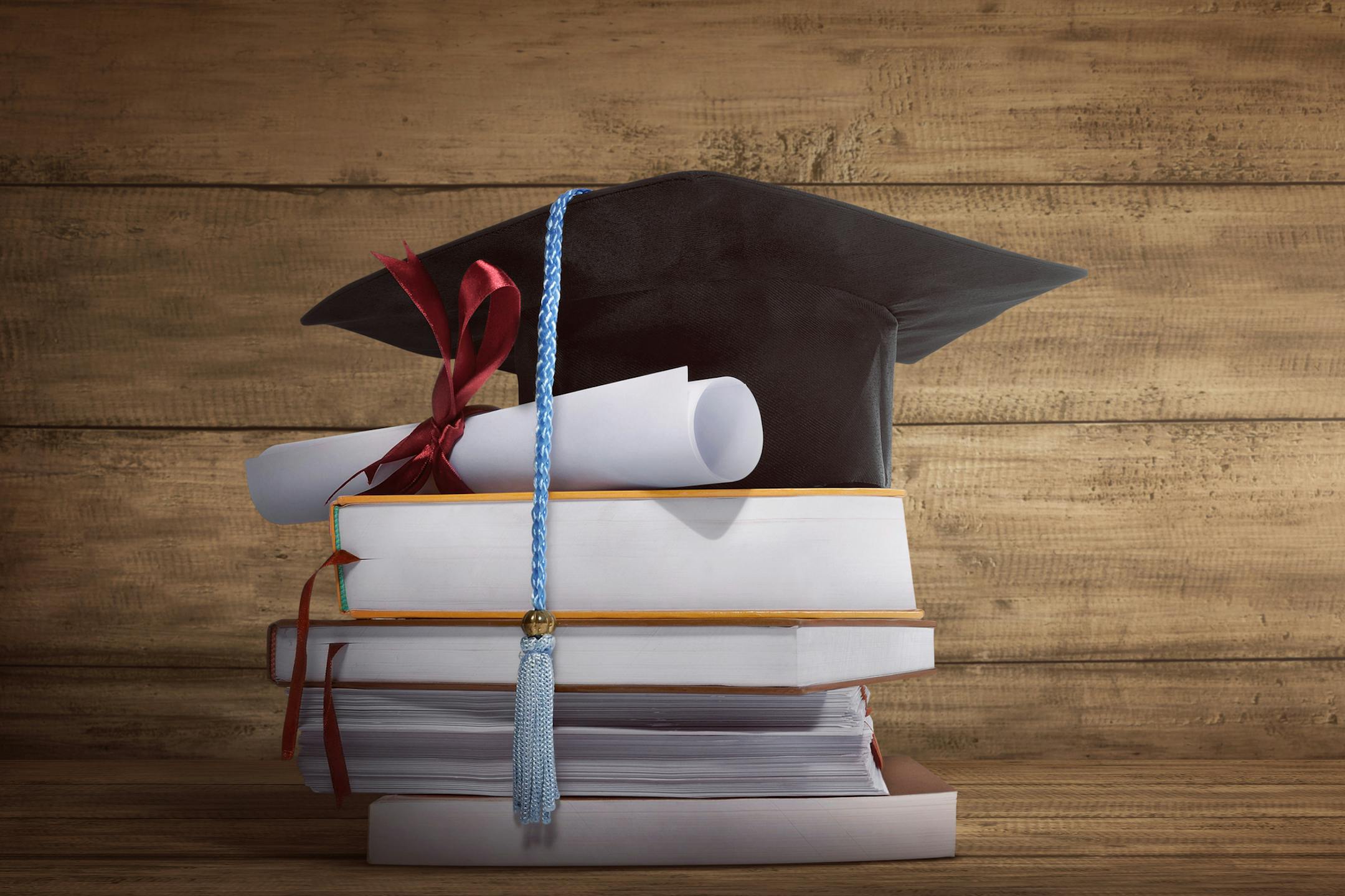 Graduation cap with graduation paper on a stack of book over wooden background
