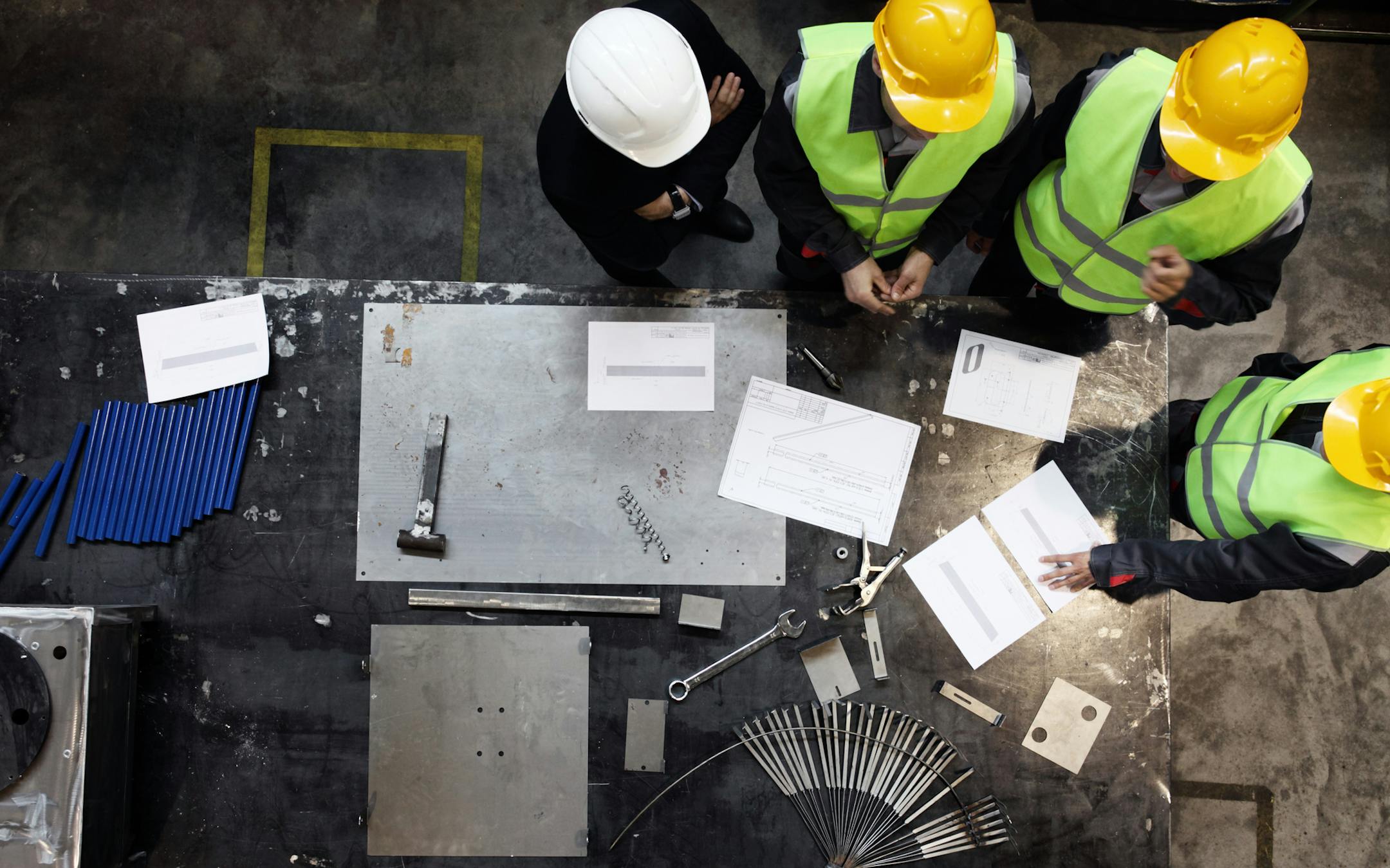 Workers and manager in safety helmets working with documents at factory