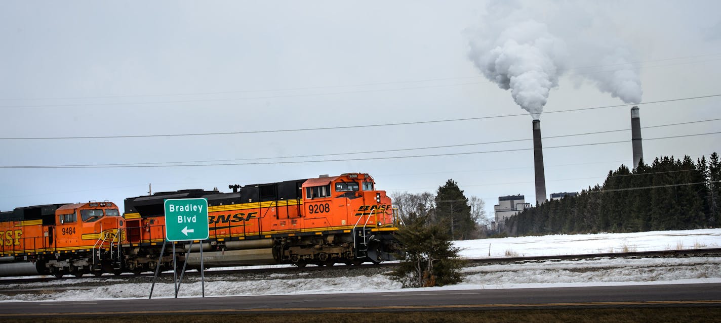 A BNSF Railway train waits on the tracks near Becker, Minn. with the twin smokestacks of Xcel Energy&#x2019;s coal-fired Sherco power plant emitting smoke in the background. The power plant relies on three trainloads of Powder River Basin coal each day. Rail delays, especially on BNSF, have slowed deliveries of coal, ethanol, grain and other commodities in recent months. Xcel said the delays have &#x201c;put a strain on coal inventory&#x201d; but its plants are operating well. Some utilities hav