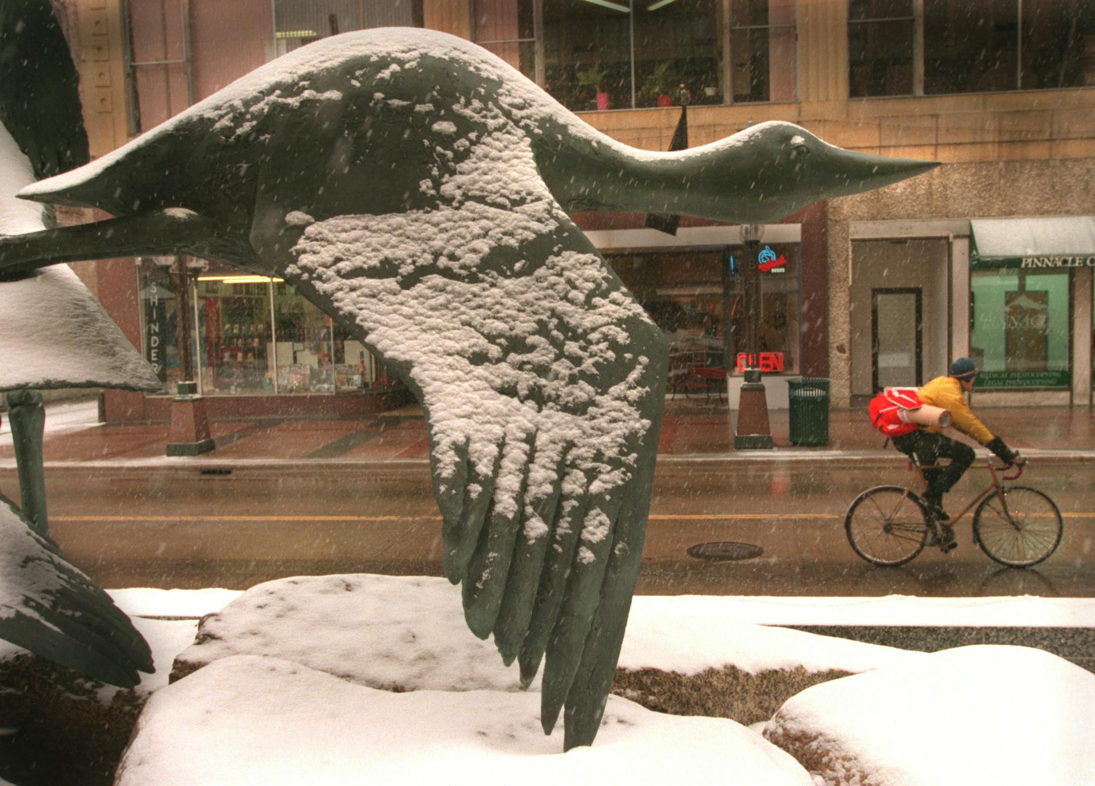 -- Cyclist rides on Nicolett mall during snowfall framed in a sculpture of a loon in flight...A winter storm is expected to drop 5 - 8 inches of snow by this afternoonÌs rush hour.The sculpture is a water fountain sculpture created by Elliot Offner and features 3 minnesota birds the Sage Groose,Great Blue Heron and Loon.