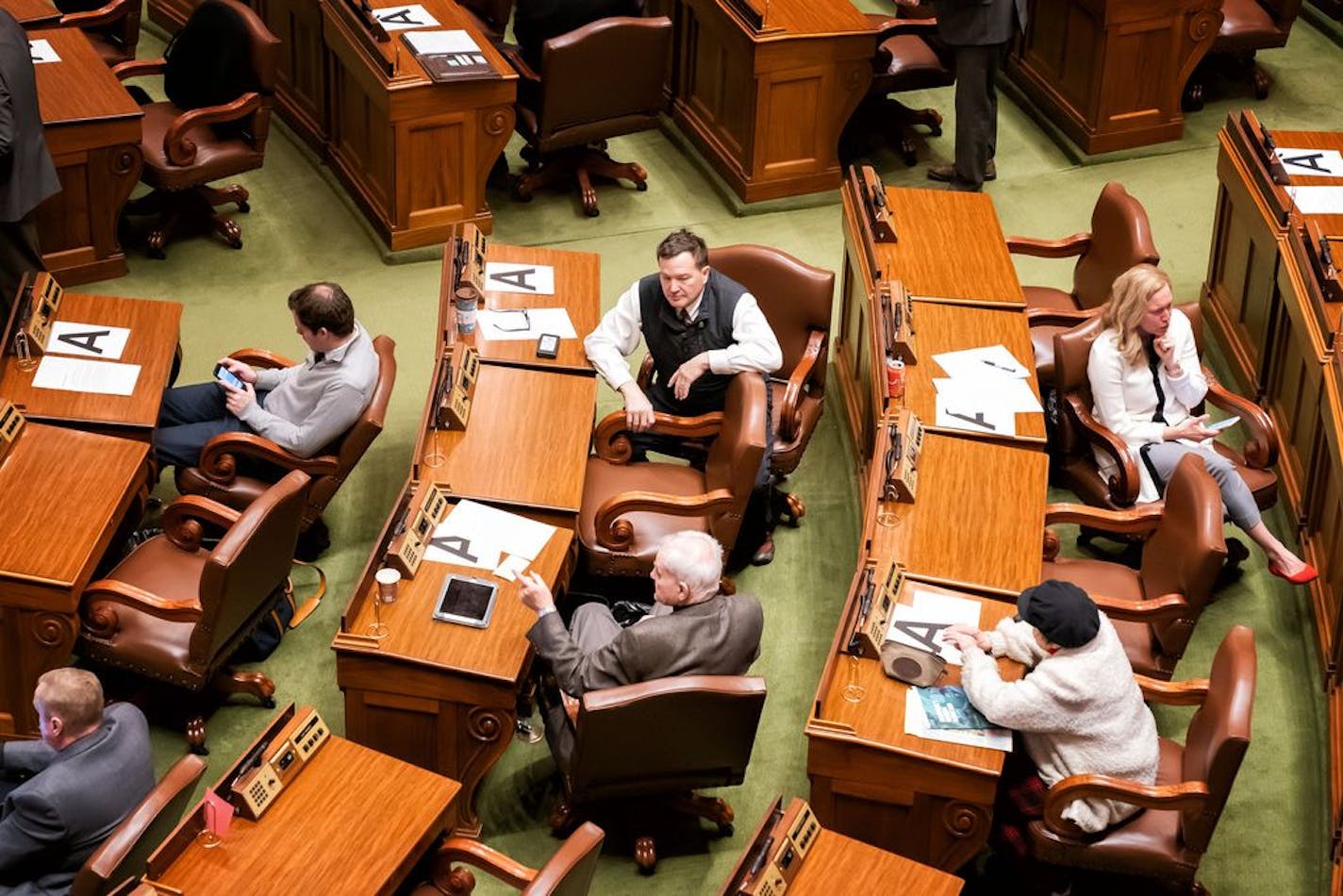 Desks and chairs where Minnesota Legislators were allowed to sit, were marked with a letter A, in order to keep them six feet away from each other, forcing some to sit in the visitors gallery and in the alcoves at the back of the chamber. Today they are all asked to be on call within an hours notice.