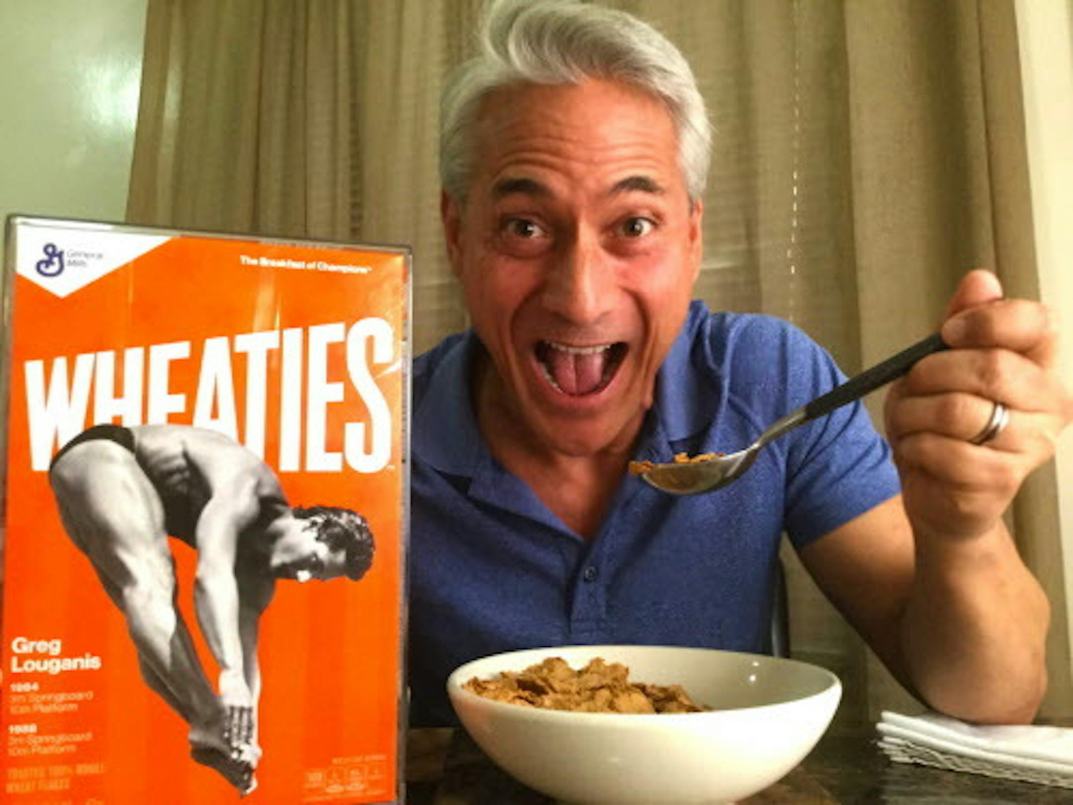 This image released by CW3PR shows former Olympic diver Greg Louganis posing with Wheaties cereal next to a commemorative box featuring him on the cover at his home on Tuesday, April 5, 2016, in Beverly Hills, Calif. Louganis, swimmer Janet Evans and hurdler Edwin Moses are on the cover of Wheaties boxes decades after their Olympic-champion careers ended. General Mills says the trio will be honored on cereal boxes as part of the Wheaties Legends series. The boxes will be on stores shelves in the