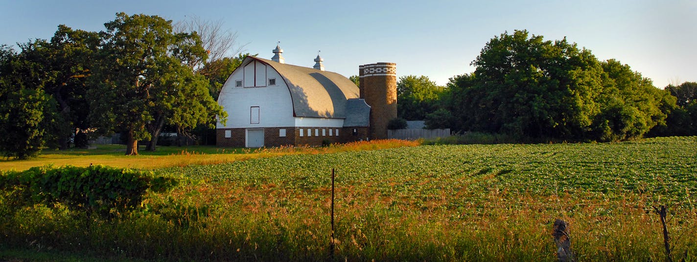 The white-and-tan arch-roof barn and attached silo stand in full view of passing traffic as an icon of a by-gone era.